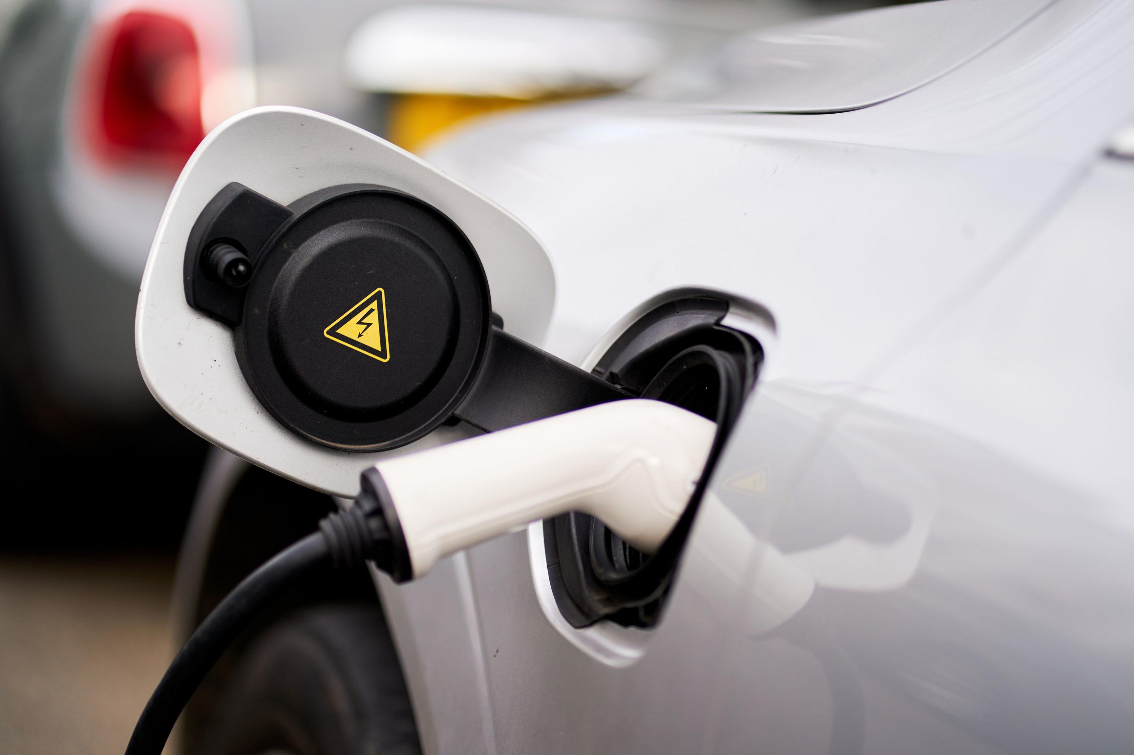 A white car with a charged going into an open slot at the side with a yellow lightning sign indicating there is electricity going in