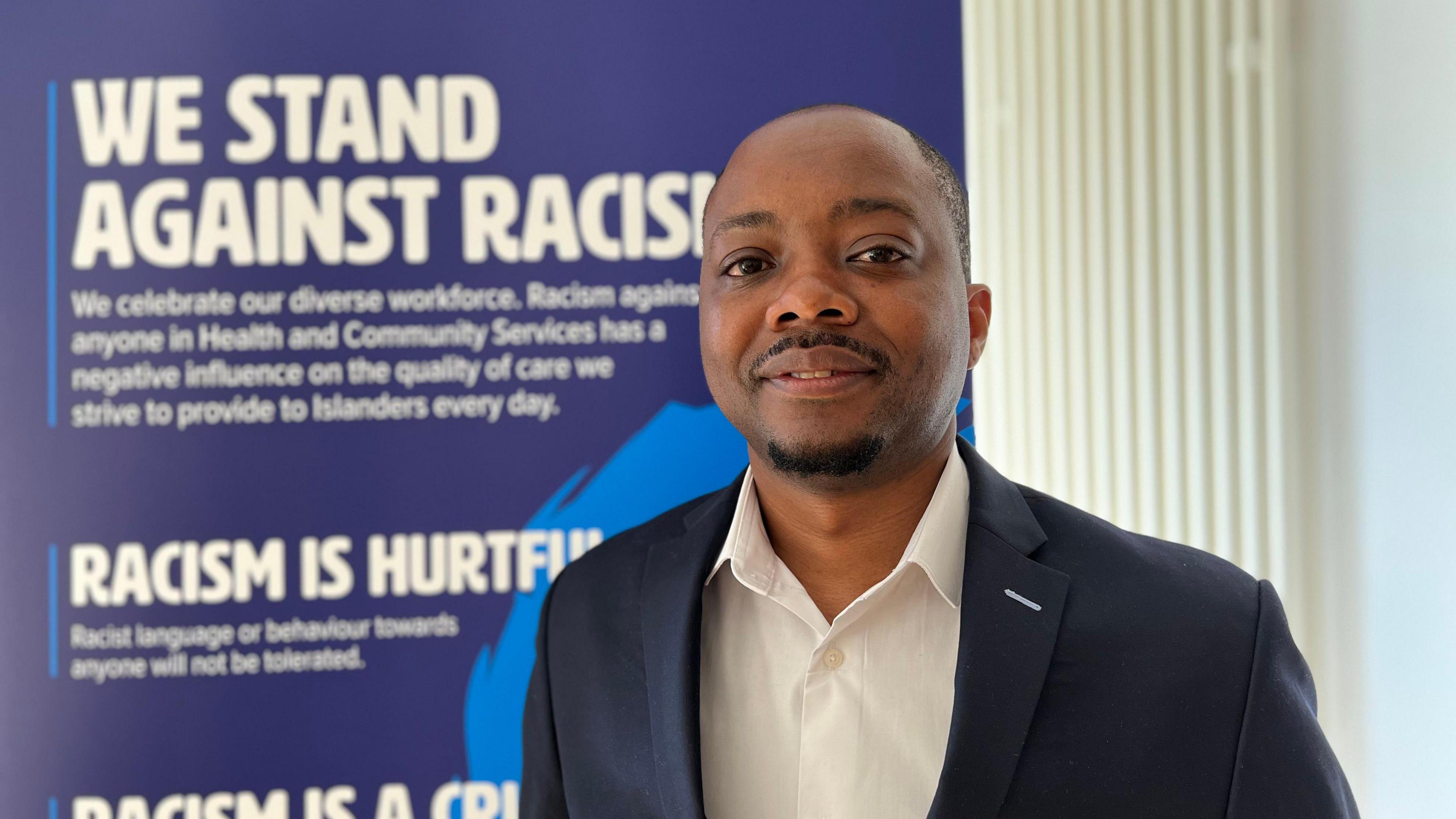 Washington Gwatidzo in front of a sign saying 'we stand against racism'