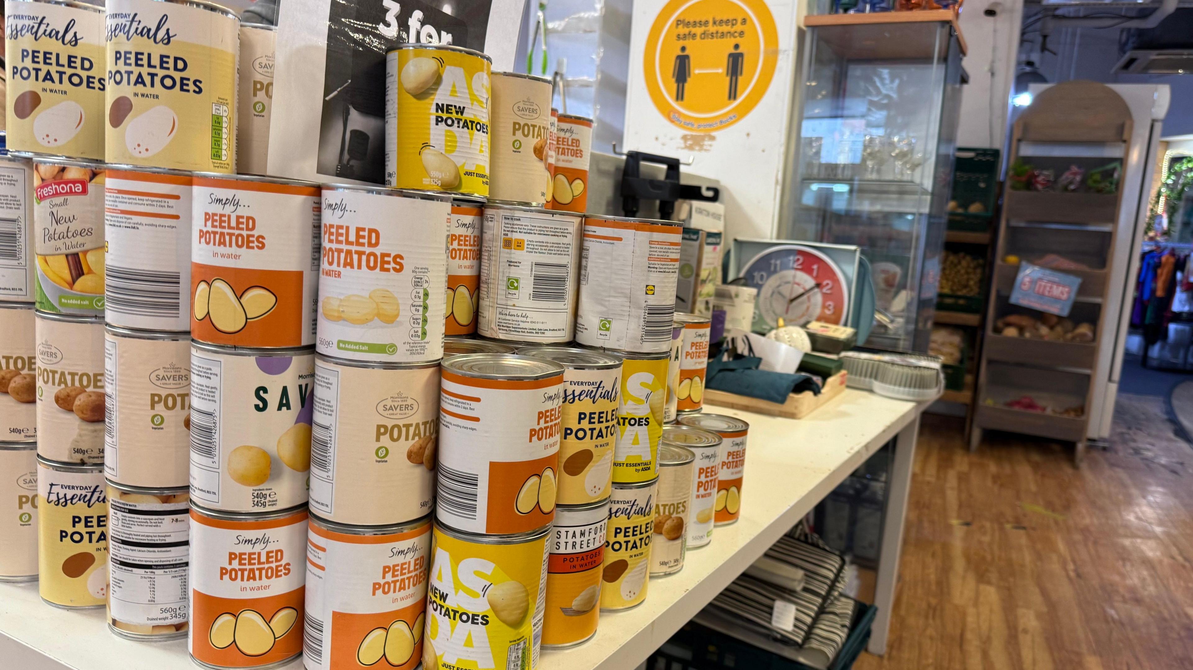 Tins of food, mostly peeled potatoes, are stacked on a table in a shop