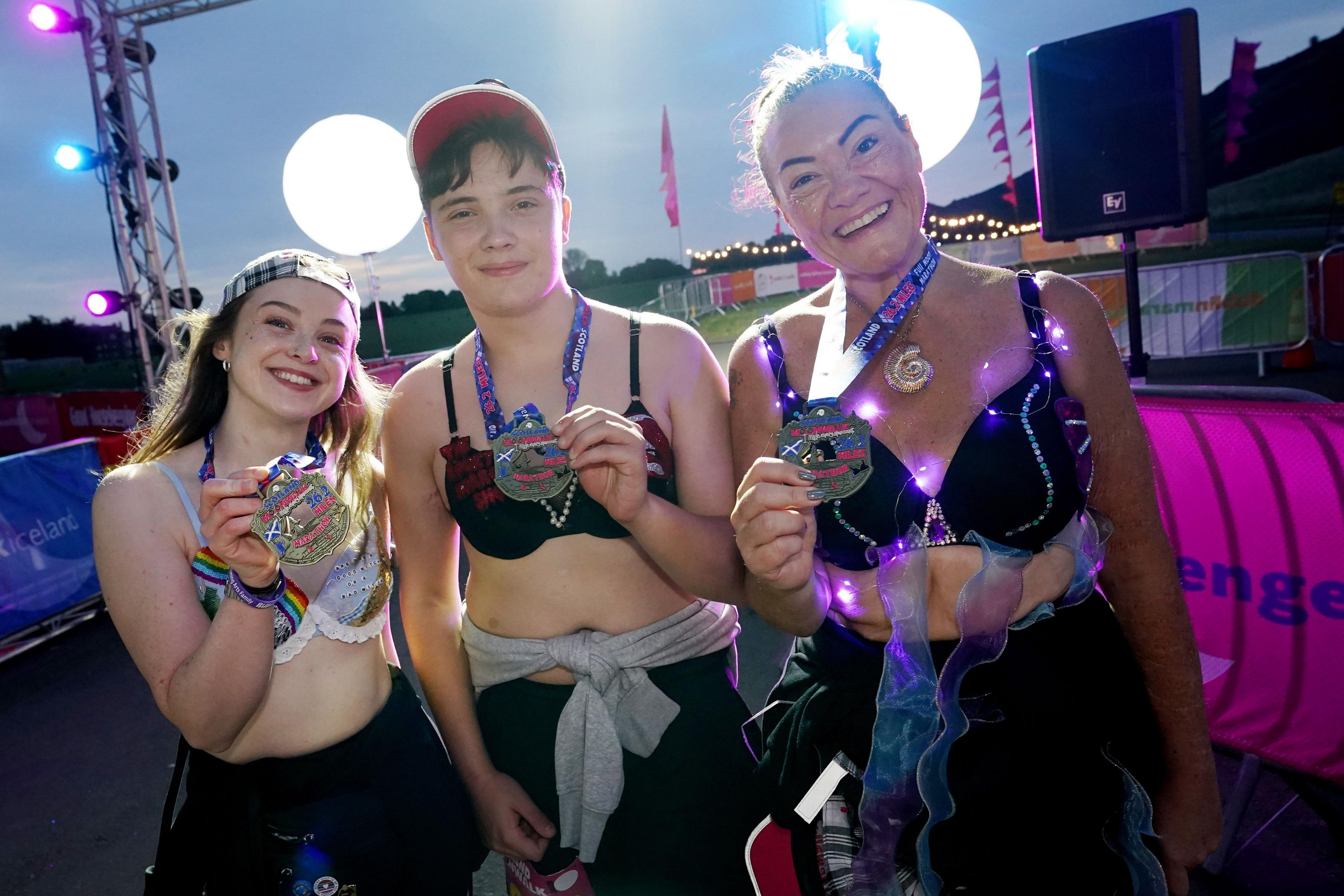 Three walkers in their bras hold up medals, smiling, having completed their challenge