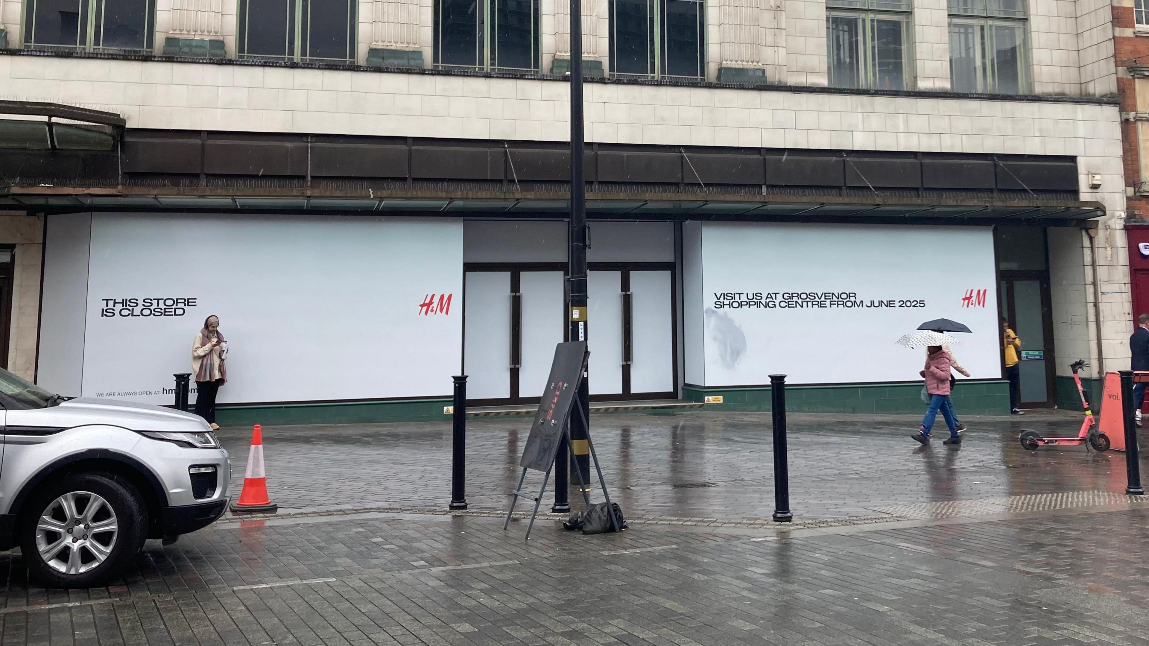 Outside view of the H&M from across the road. The building is boarded up with white signs that have H&M in red written on them.