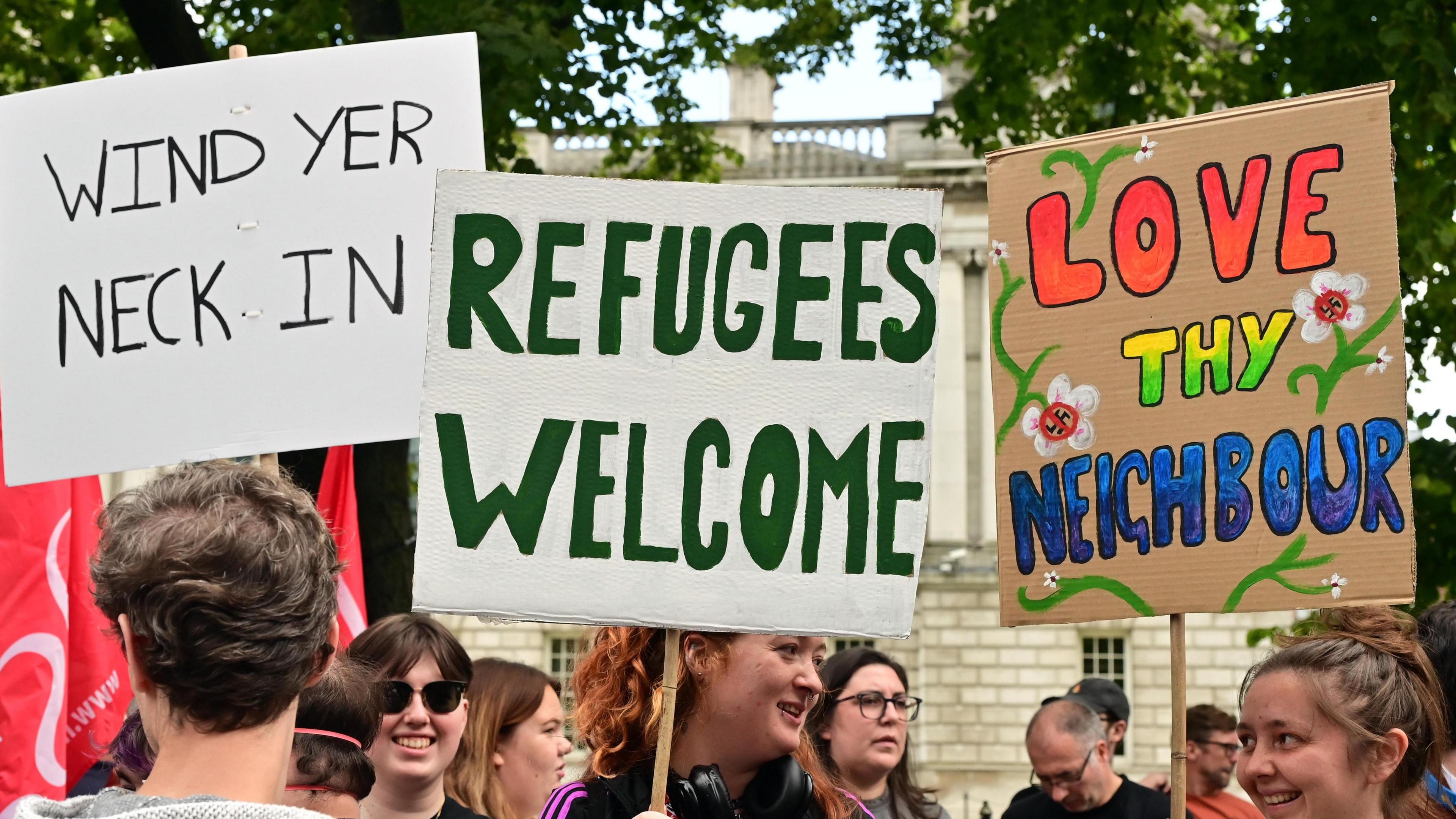 Placards saying 'wind yer neck in', 'refugees welcome' and 'love thy neighbour'