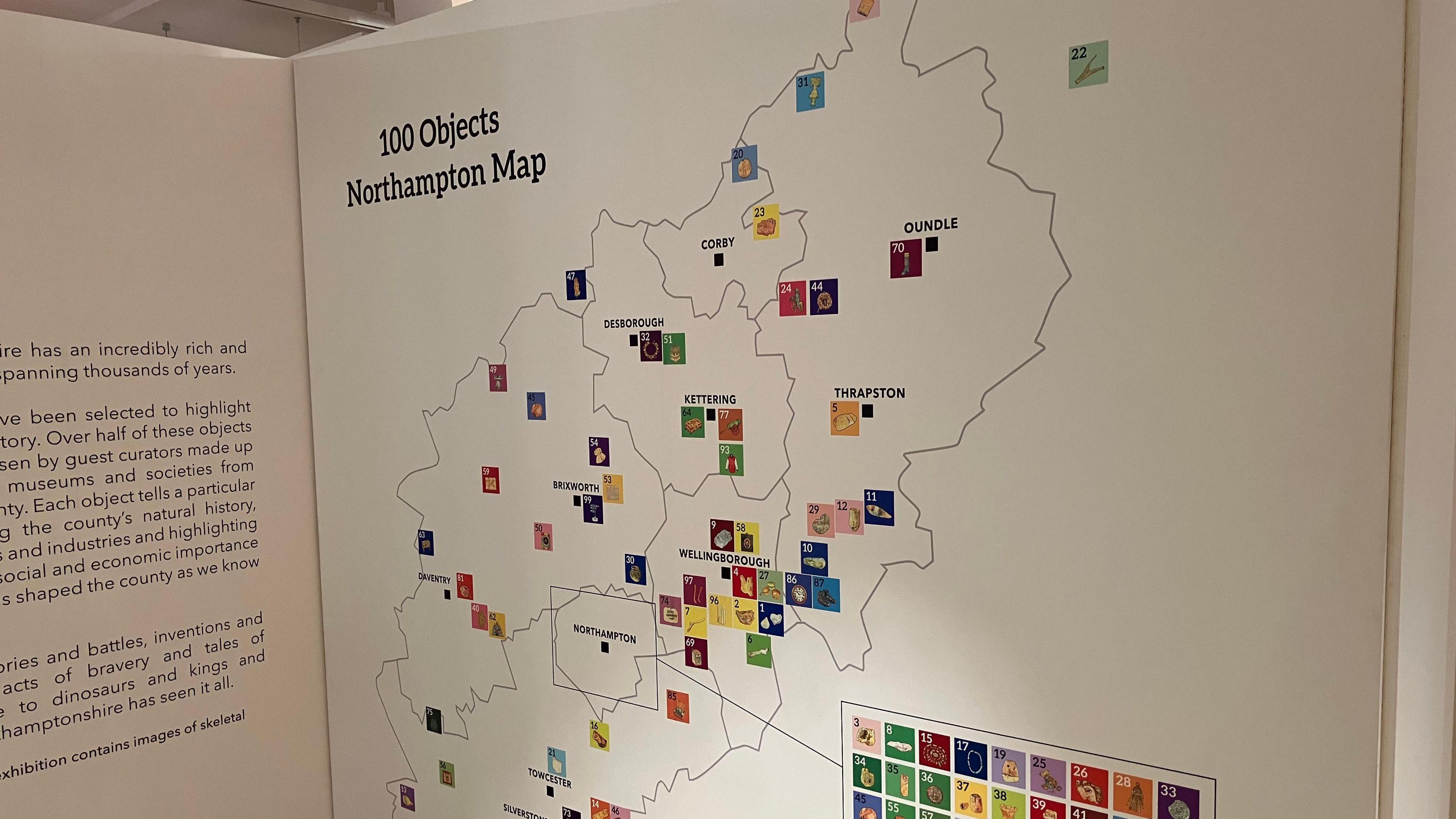 A map of Northamptonshire is detailed on a white board that is part of a museum exhibition. Small images of items can be seen all over the map.