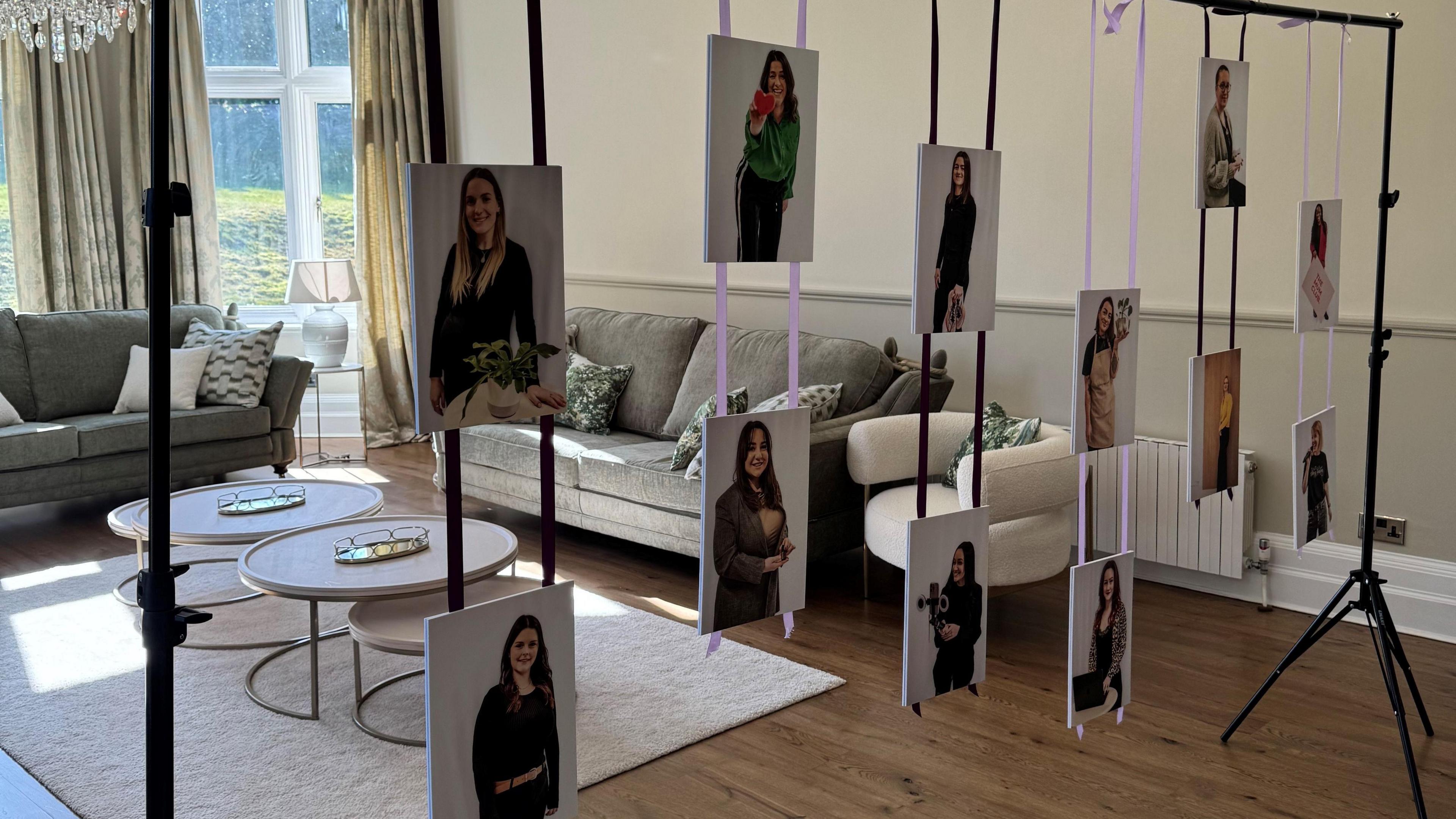 A large number of images of women dangling off threads of fabric from a frame, situated in a room with seating and tables.