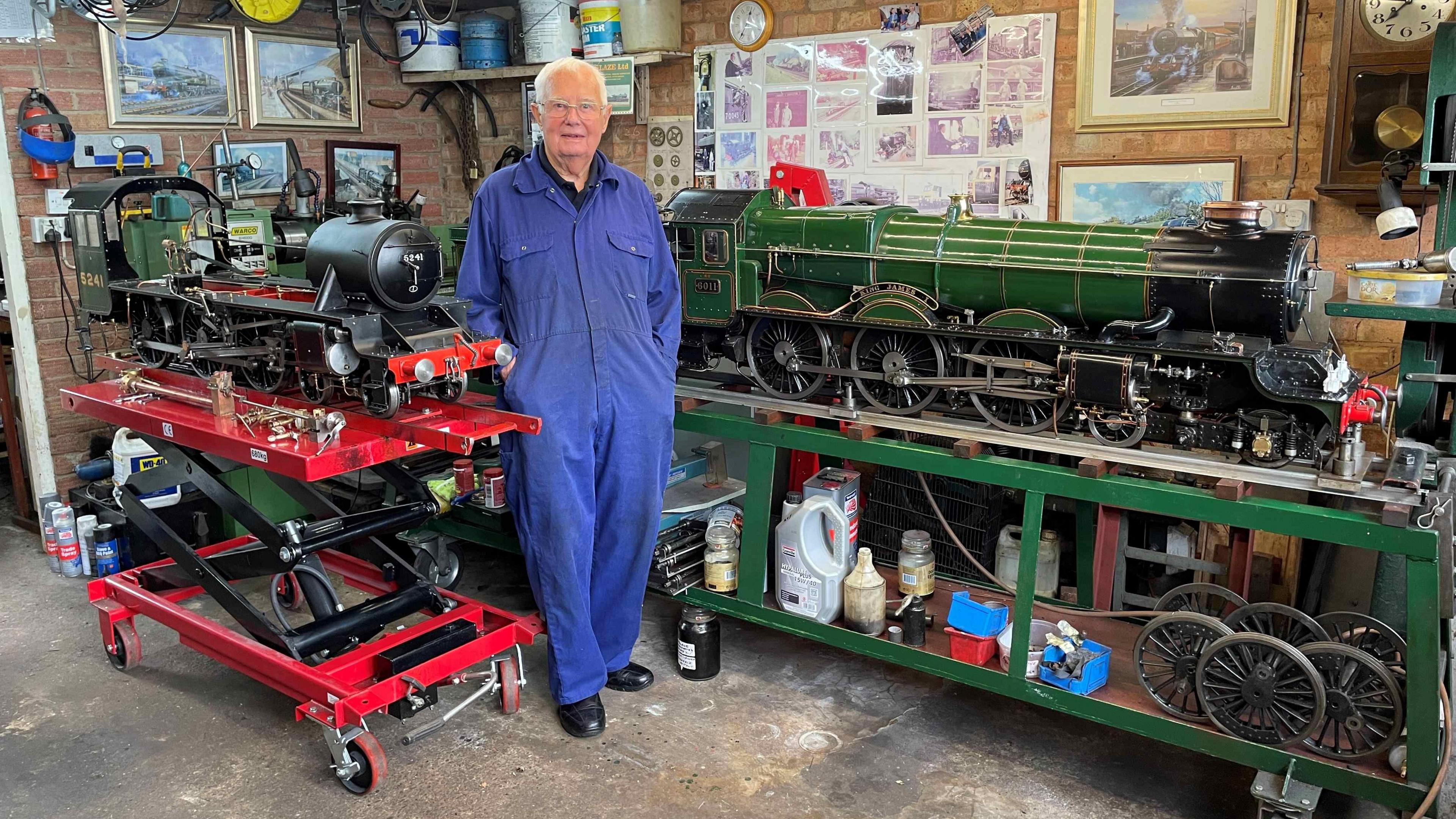 Dennis Herbert standing in a blue mechanic's suit and beside his green model of 6011 King James steam train