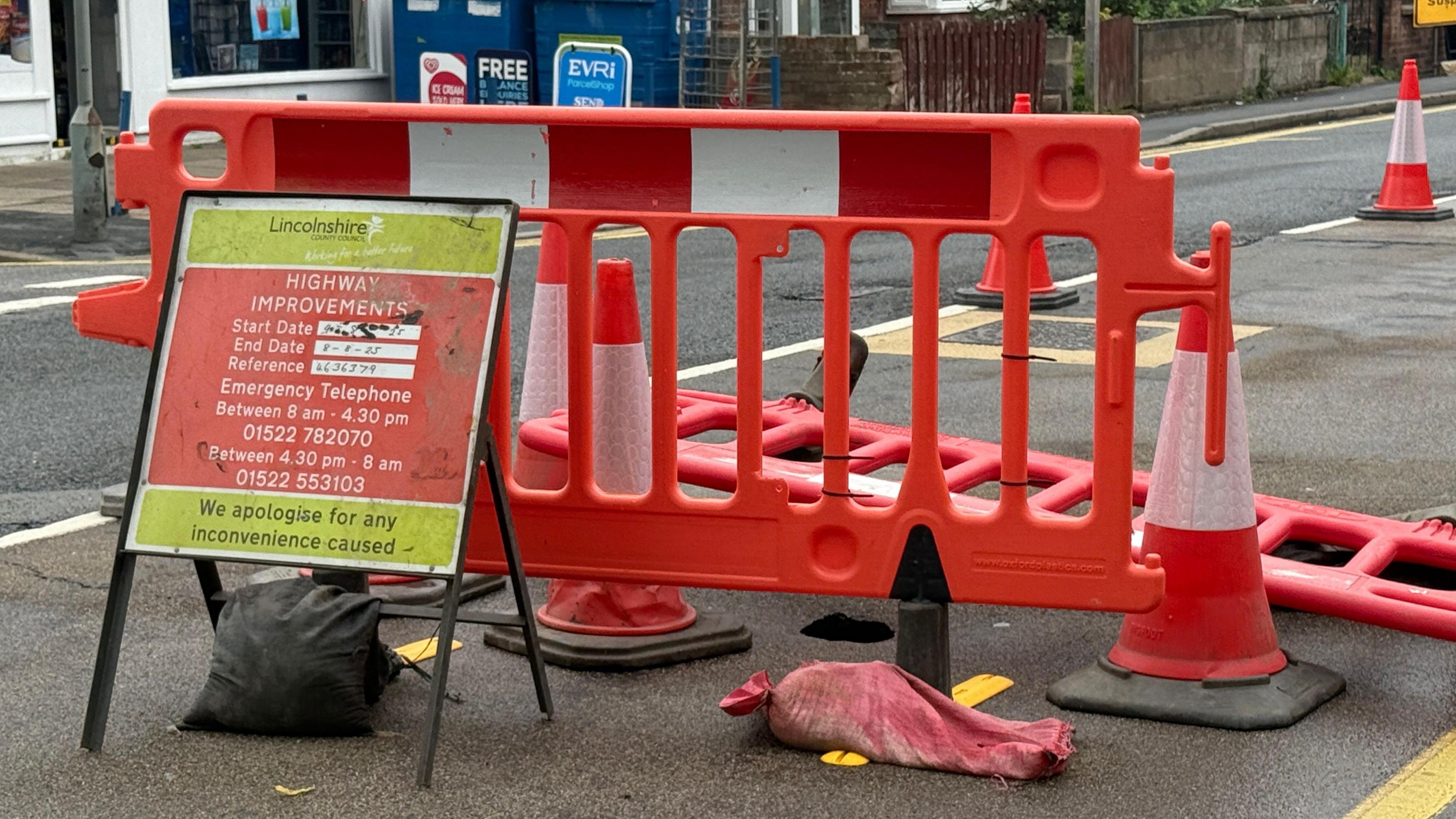 A part of a road which has been sectioned off with orange plastic barriers and orange cones. The sinkhole is beyond the barrier.