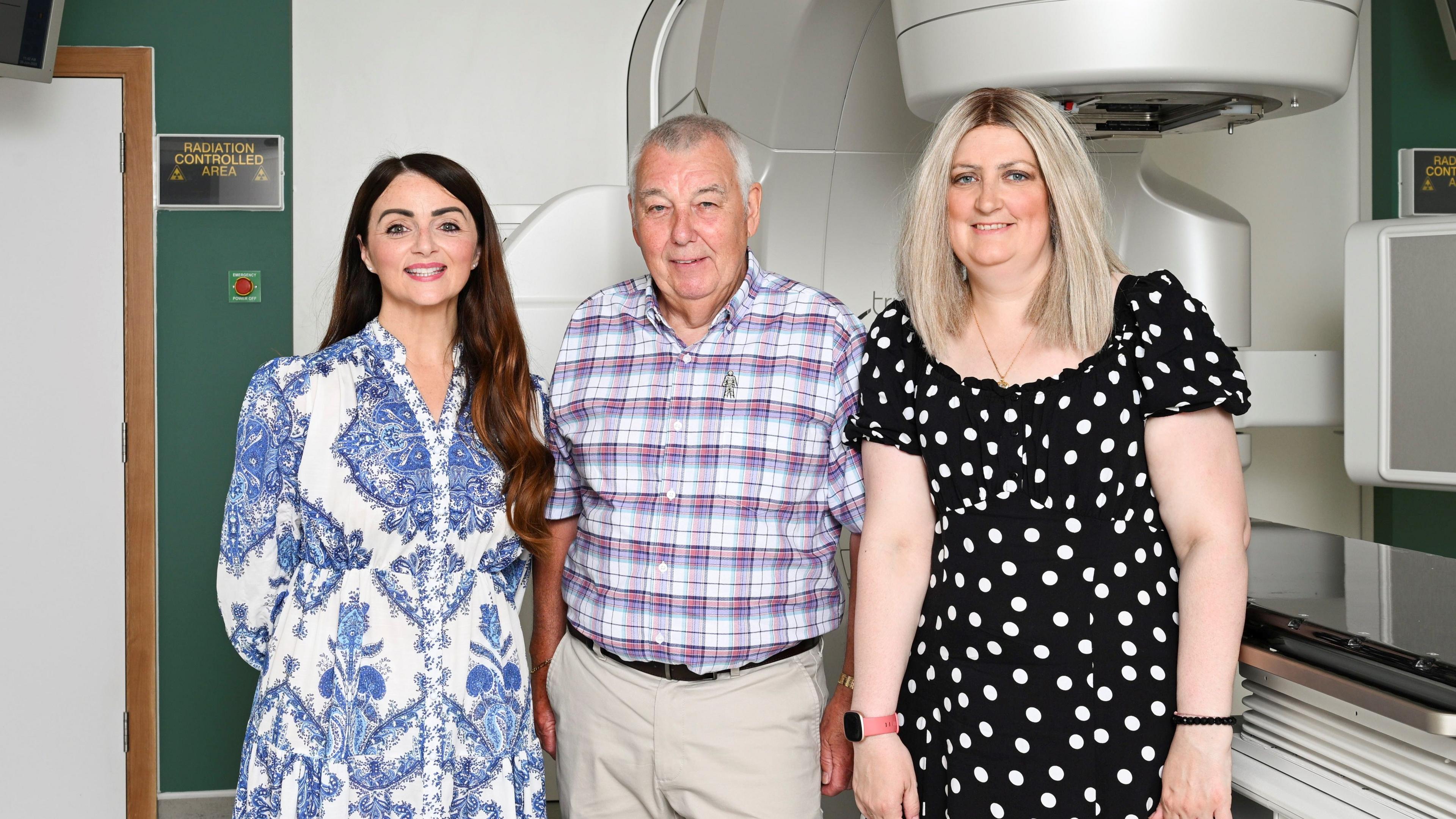Three people pose for a photo in front of cancer scanning equipment at OUH Radiotherapy @ Milton Keynes