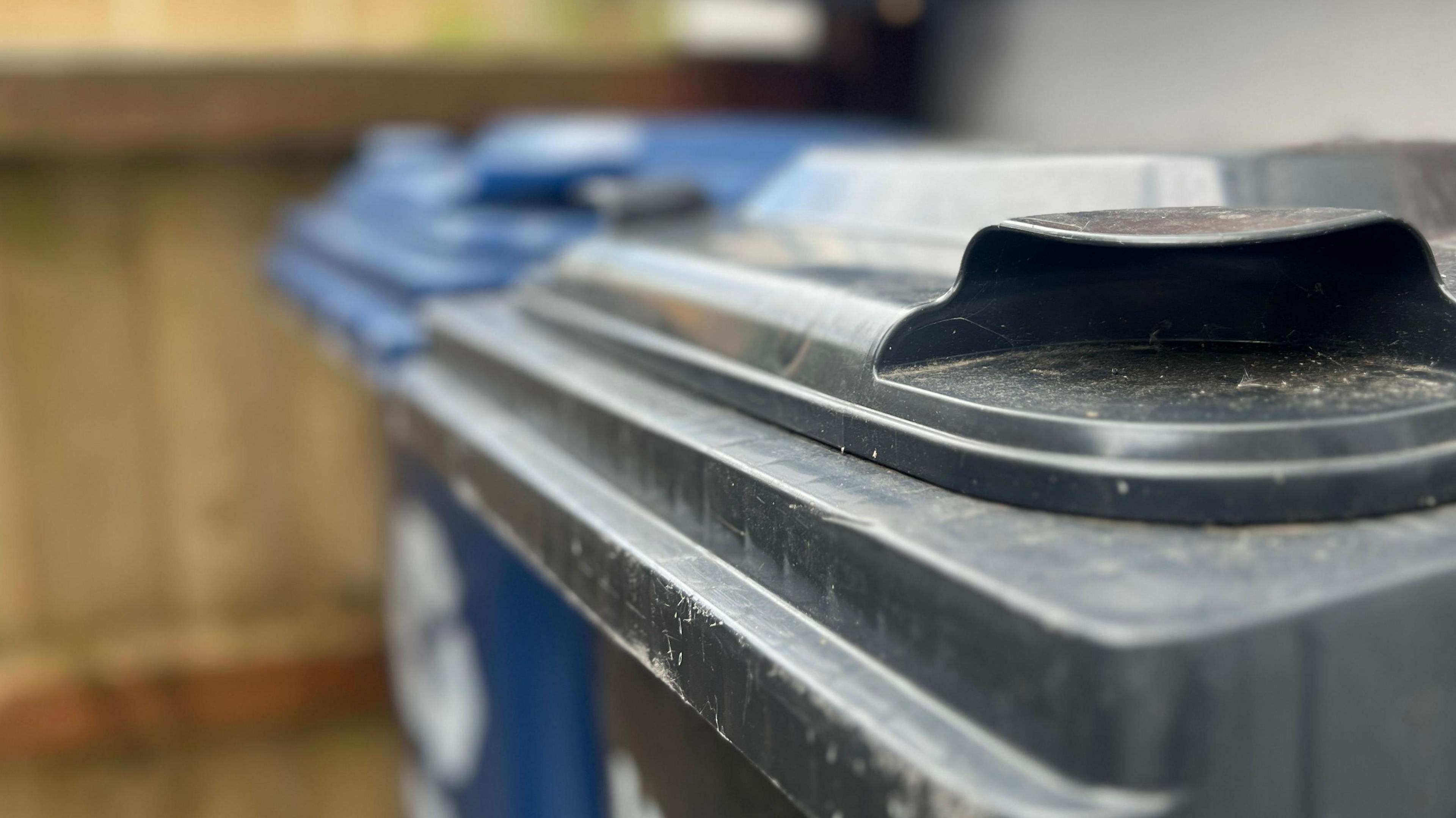 A close of up a blue and black bin. They are positioned near a wooden fence.