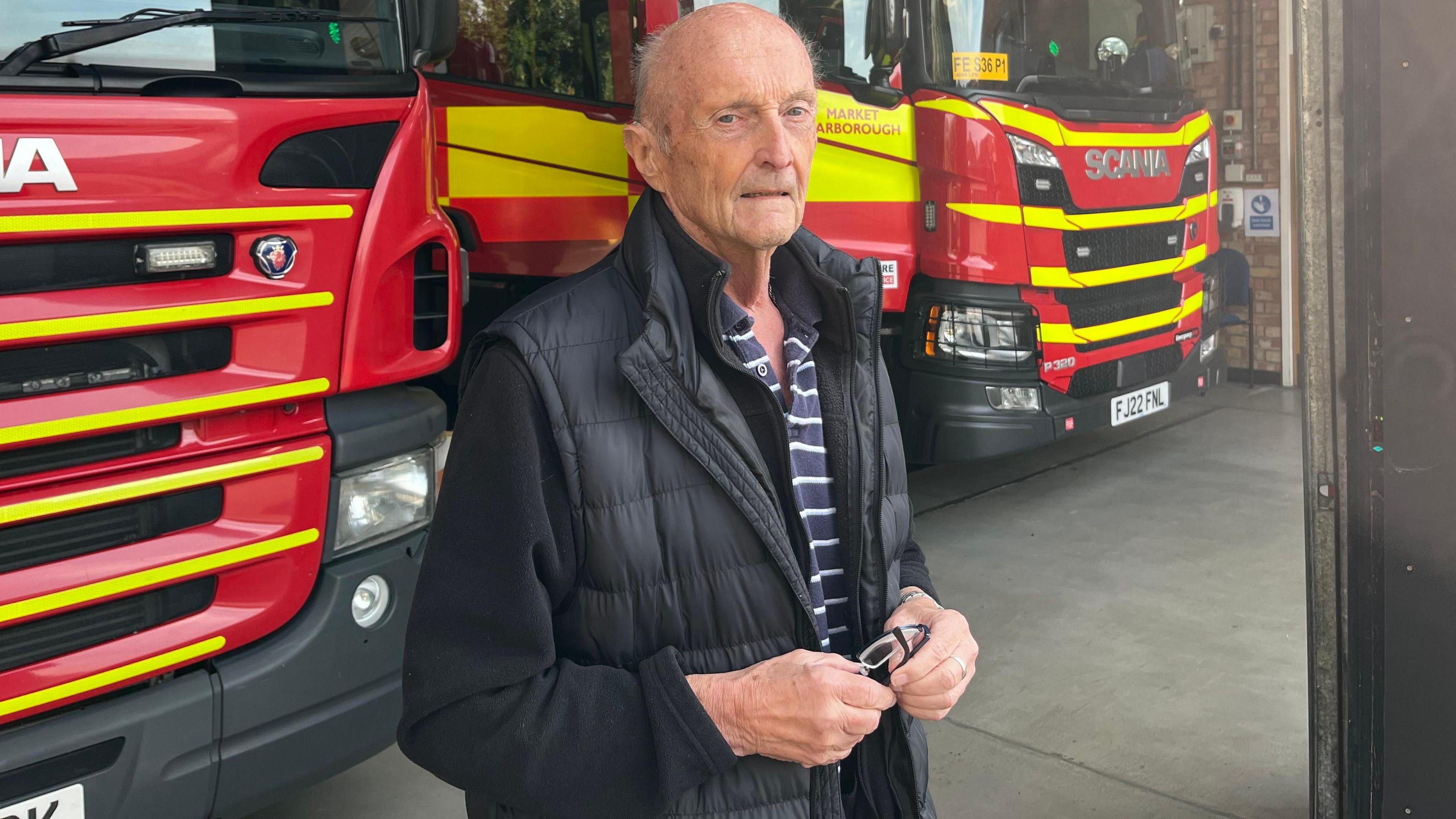 A man in his 70s standing in front of two fire appliances