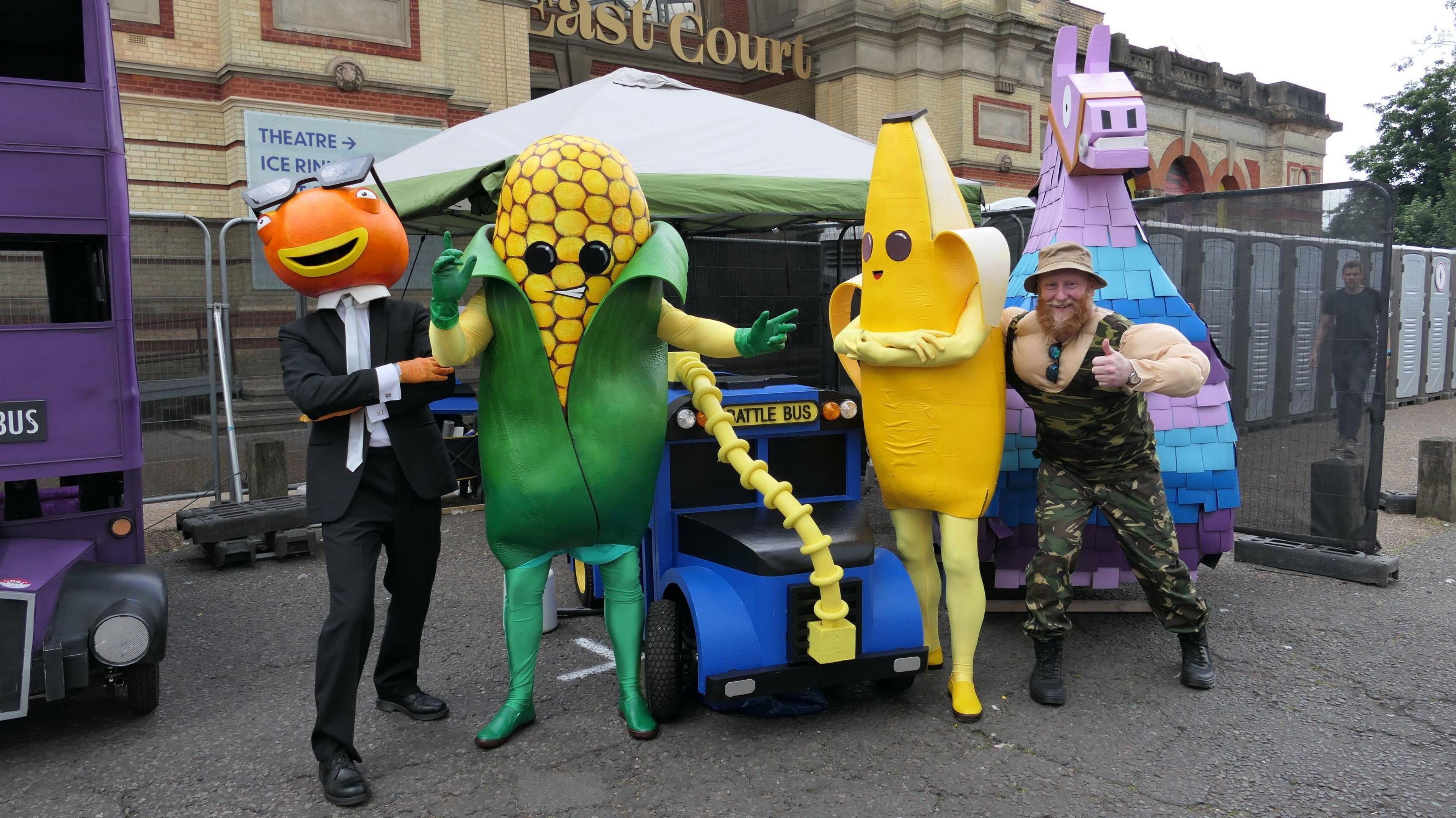 The Llama Drama teamin costumes including a banana and corn - pose outside Alexandra Palace in London