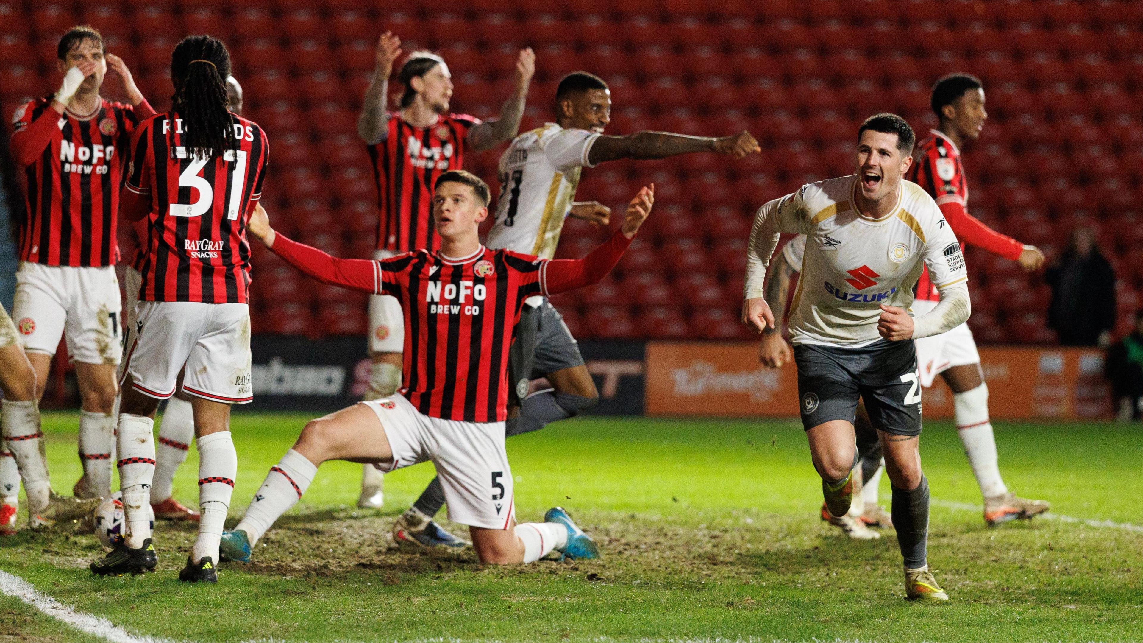 Jon Mellish runs off to celebrate after scoring MK Dons' second goal at Walsall as a number of players in red and black look exasperated 