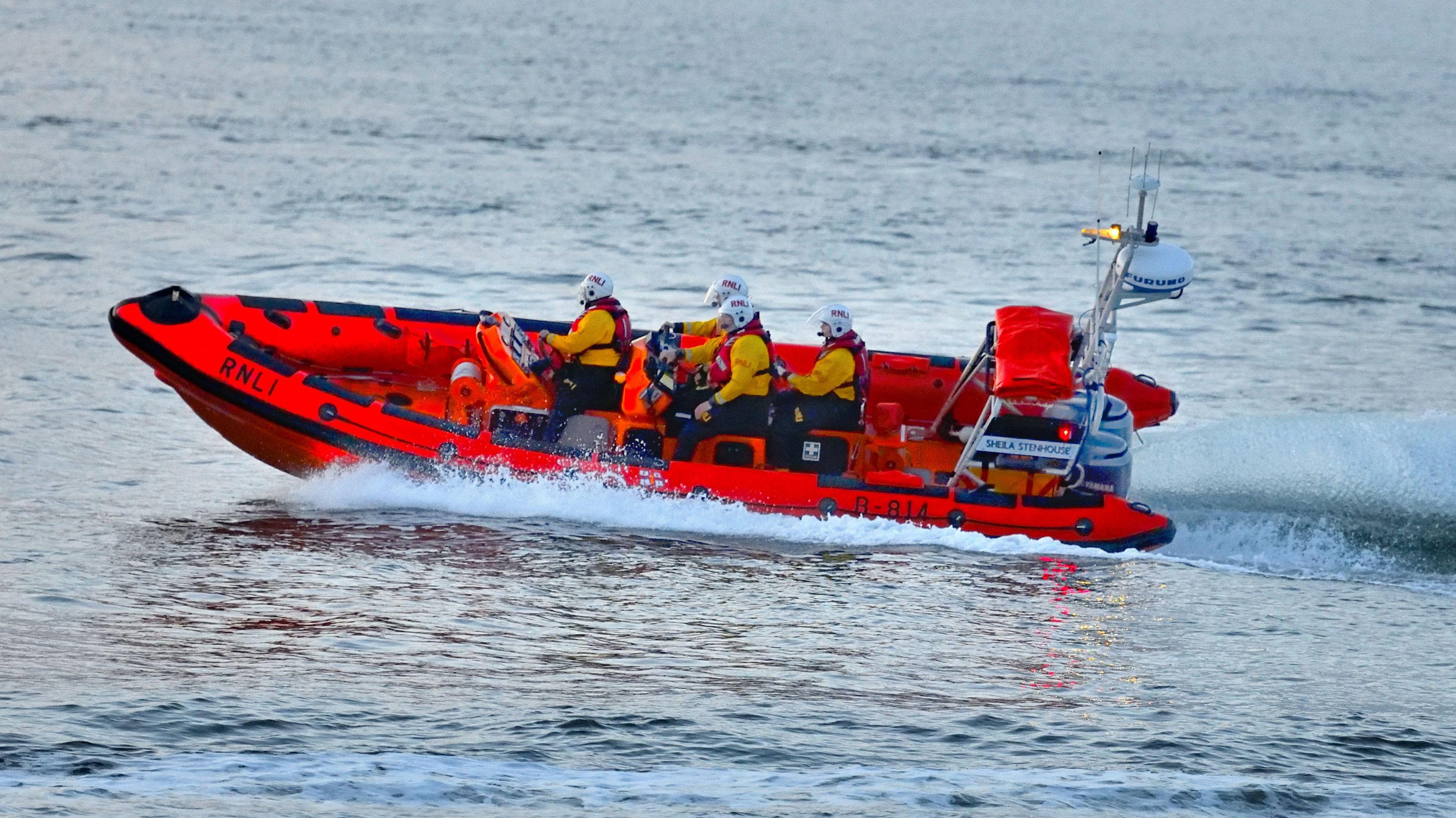 A lifeboat and its crew speed across the water leaving a big trail in the water behind them