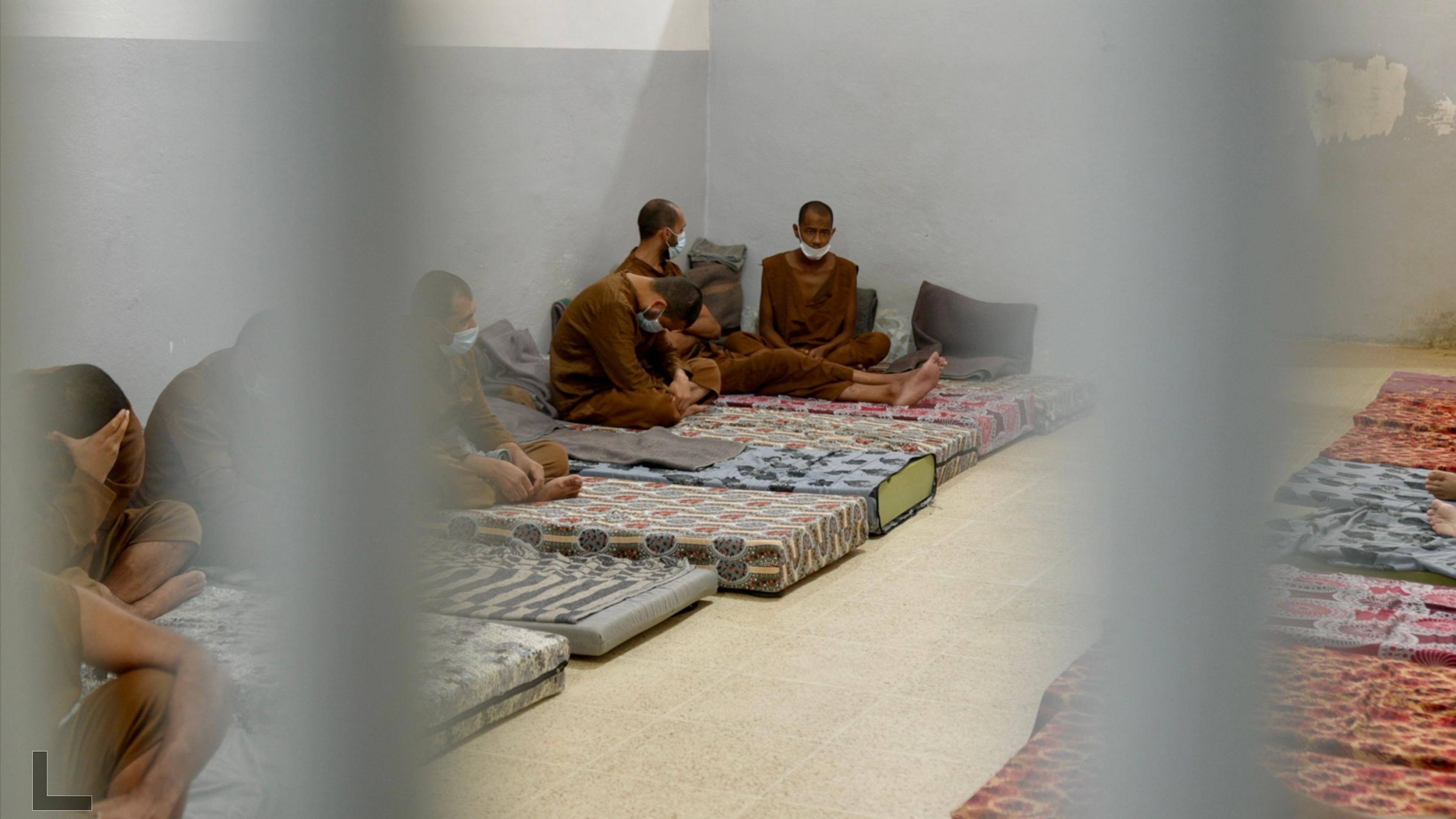 Several detainees in brown uniforms with shaven heads sitting on mattresses inside  al-Sina prison.