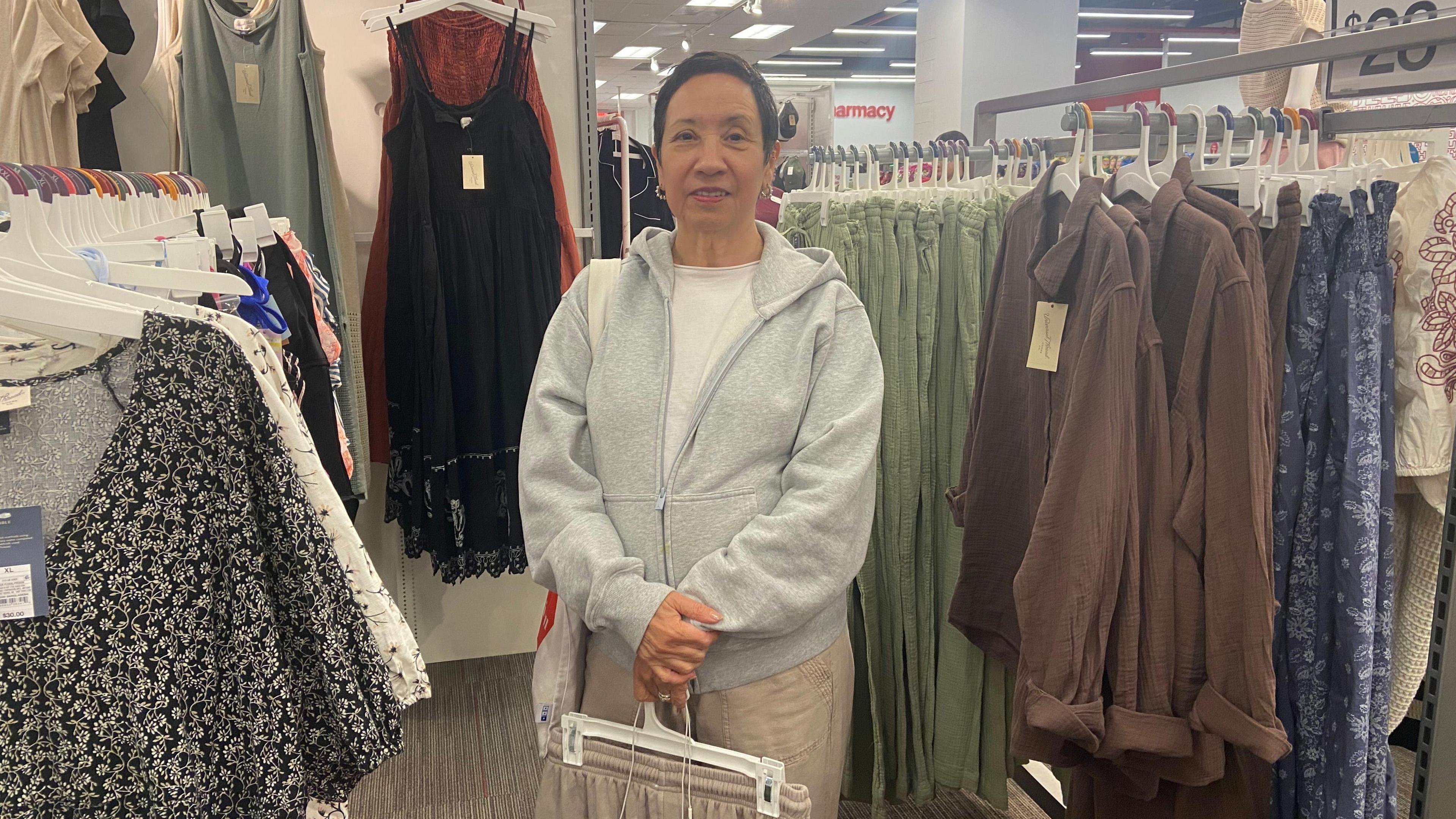 Nancy Garcia, who works in the publishing and gifts industry, shops for clothing at a Target location in Manhattan on 10 Sept 2025. She is surrounded by dresses and jackets on hangers and is holding some clothes.