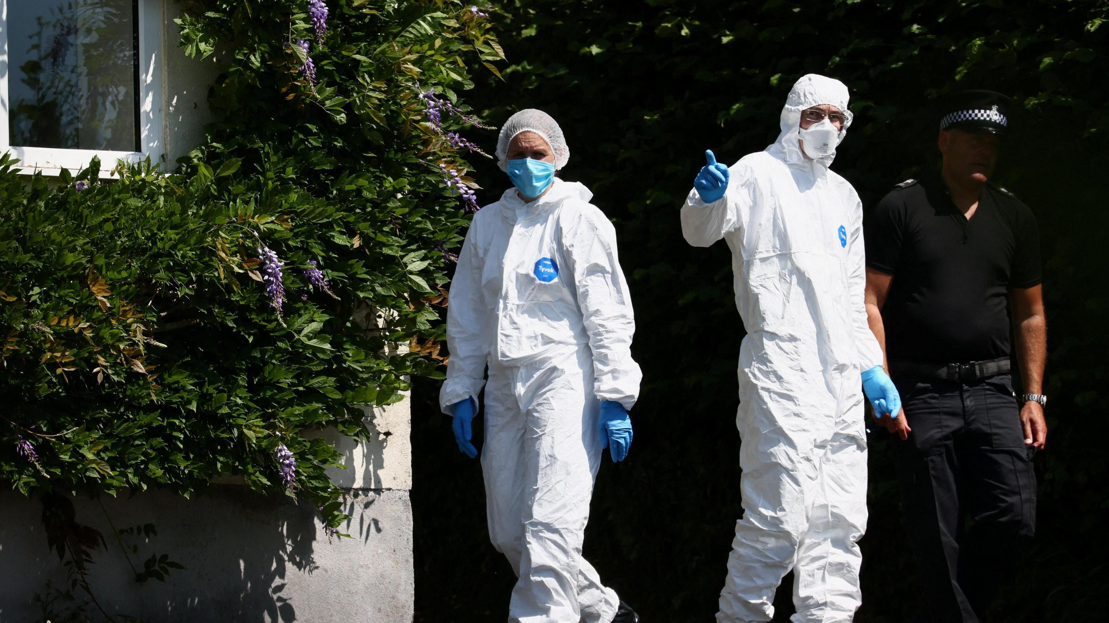 Members of the forensic team walk on site as the police investigate the home of 78-year-old former government minister.