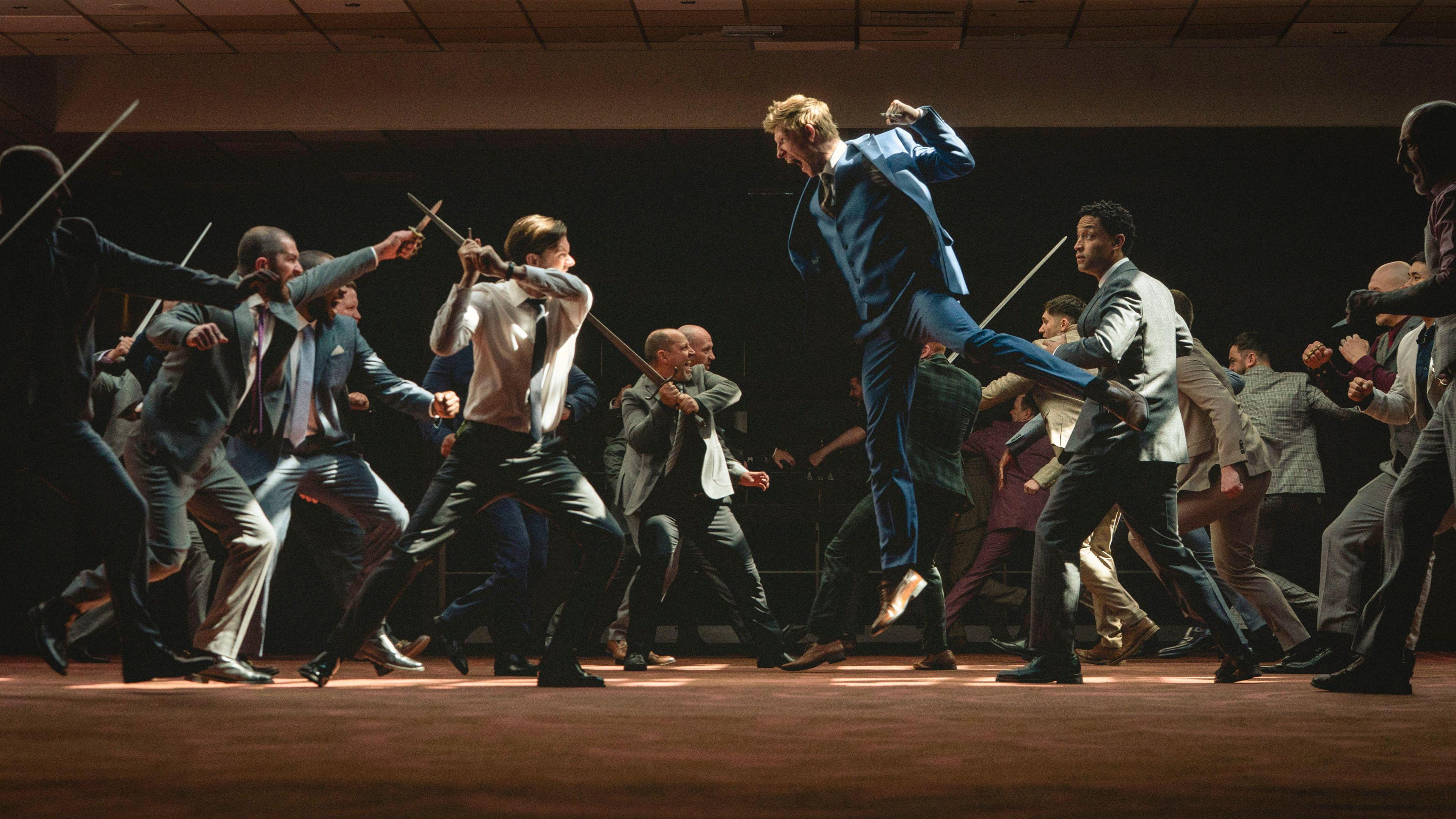 A still from a dramatic fight scene between men in suits, the colours in the picture are rich and their movements are exaggerated