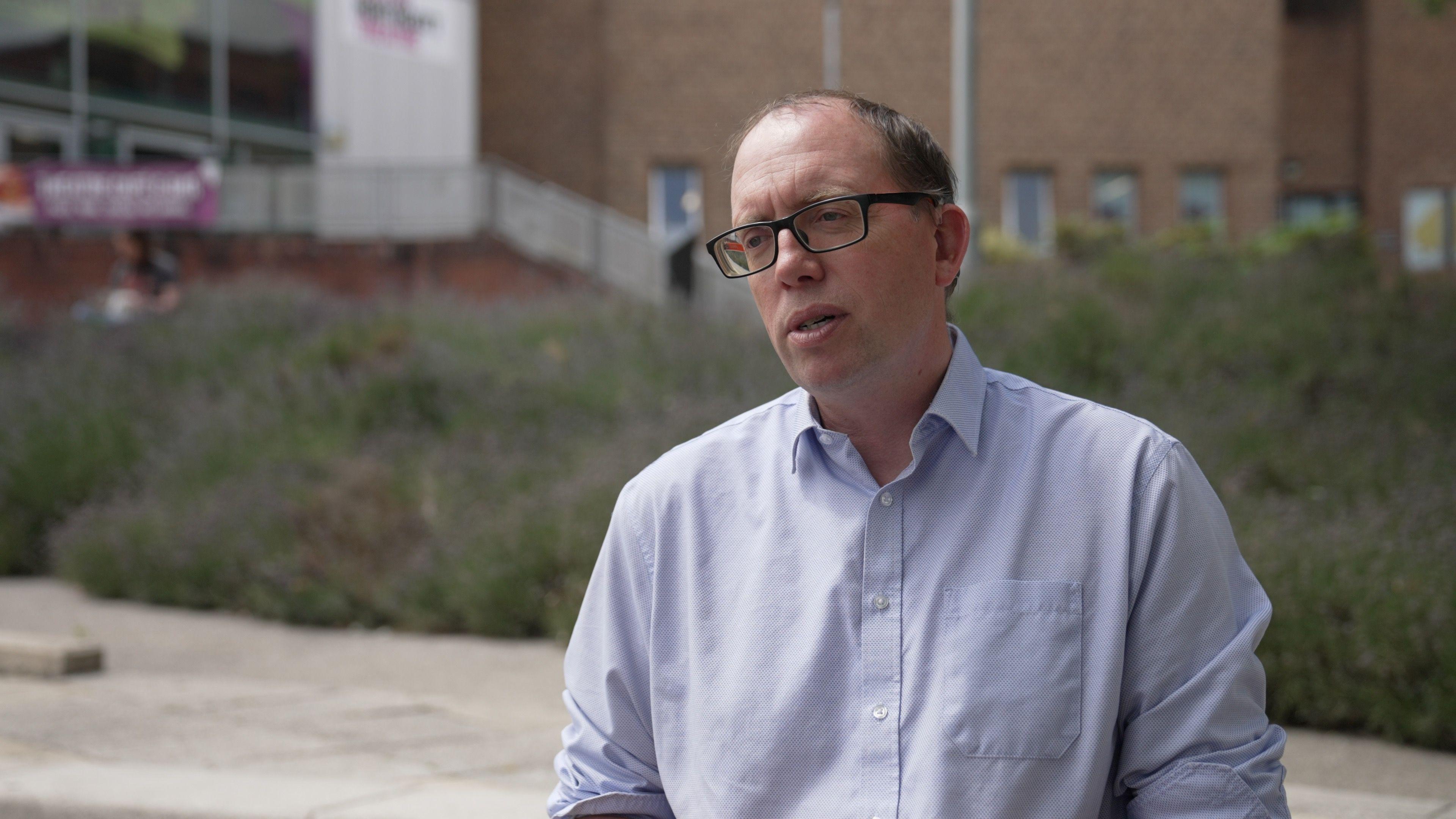 A man wearing a light blue shirt and glasses stands in front of the lavender planted outside the Northcott Theatre in Exeter.