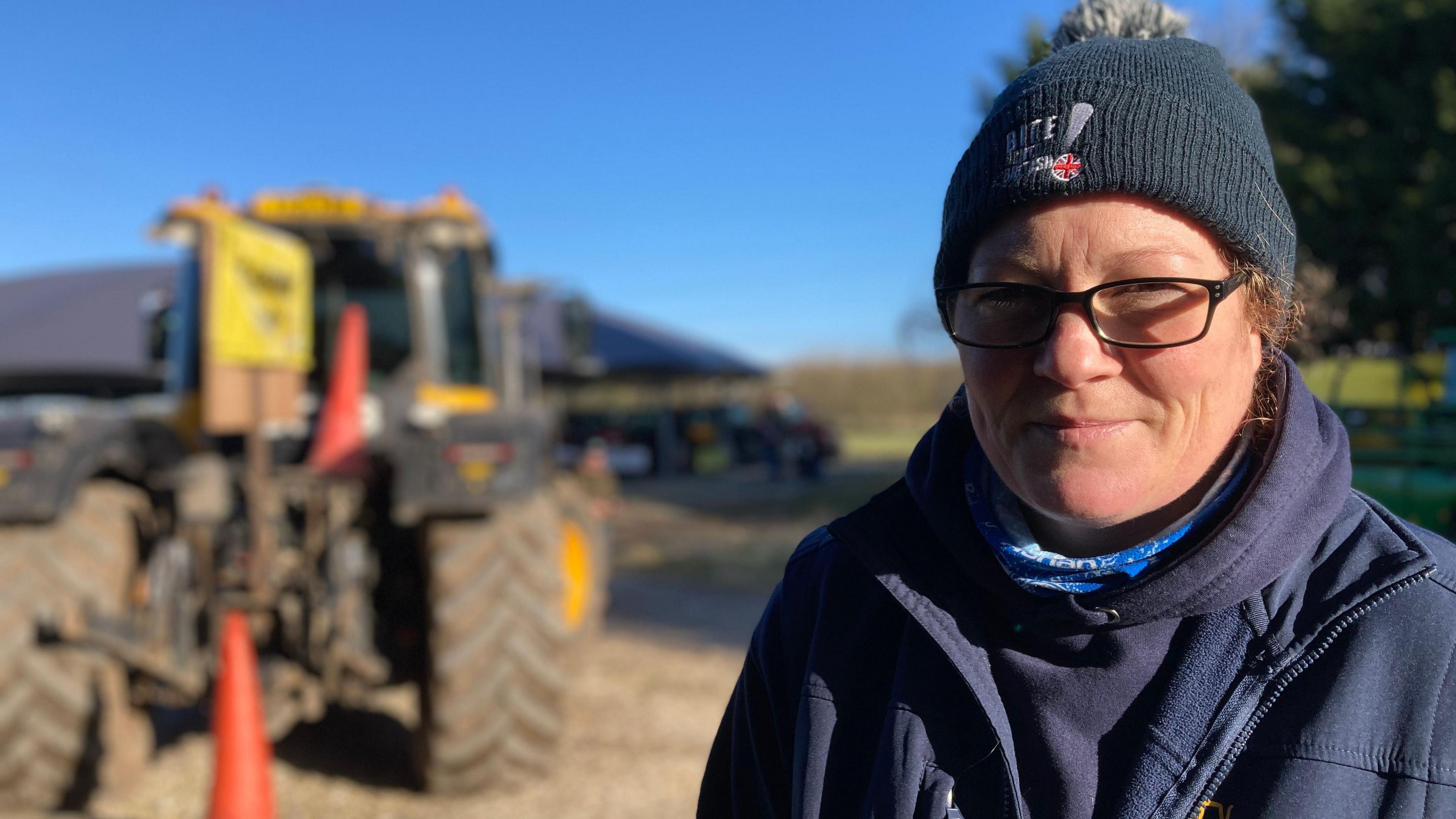 Anna Lonthorp stands infront of a tractor wearing a navy blue fleece, bobble hat and glasses.