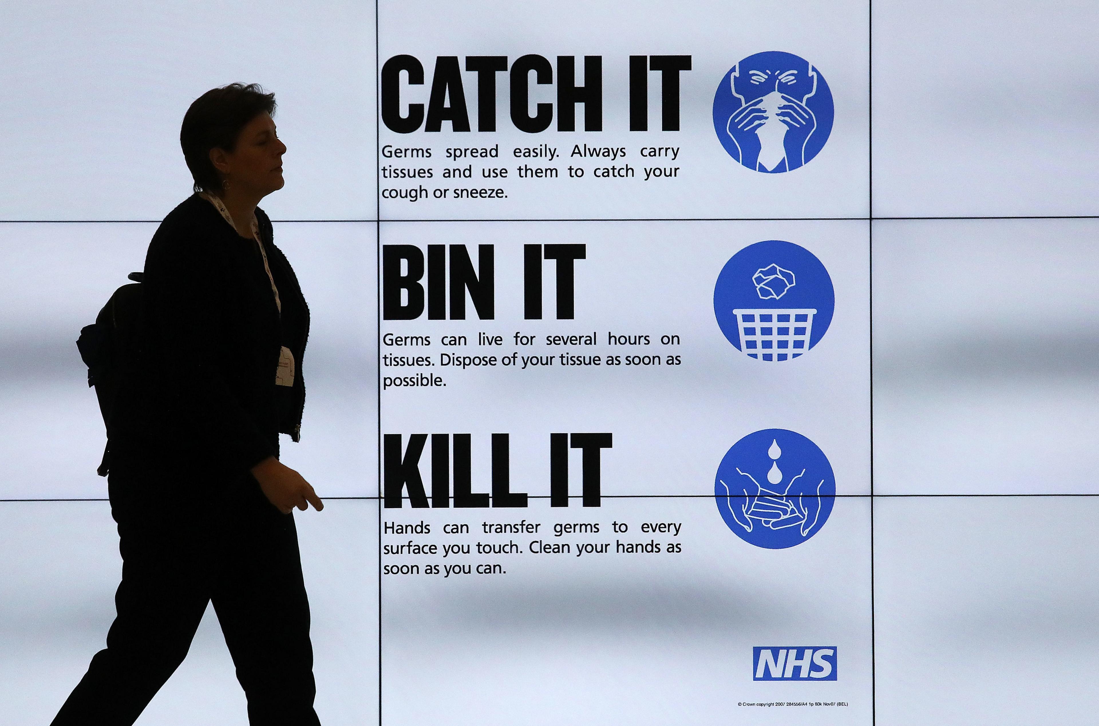 Woman walks past sign displaying public health advice