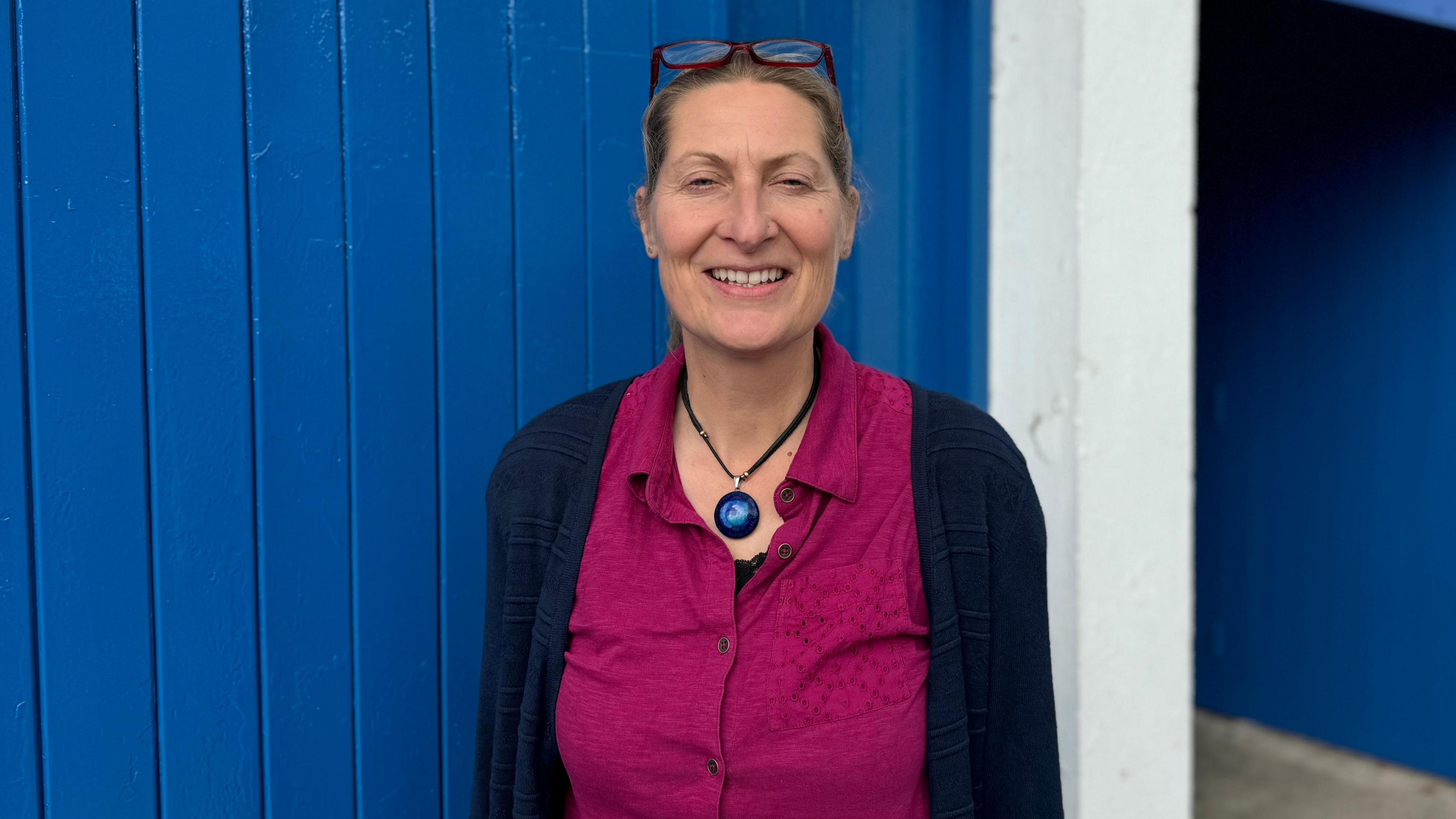 A woman named Nadine Dooley wearing a pink blouse and dark blue cardigan standing in front of a blue backdrop at Ipswich Town's Portman Road stadium