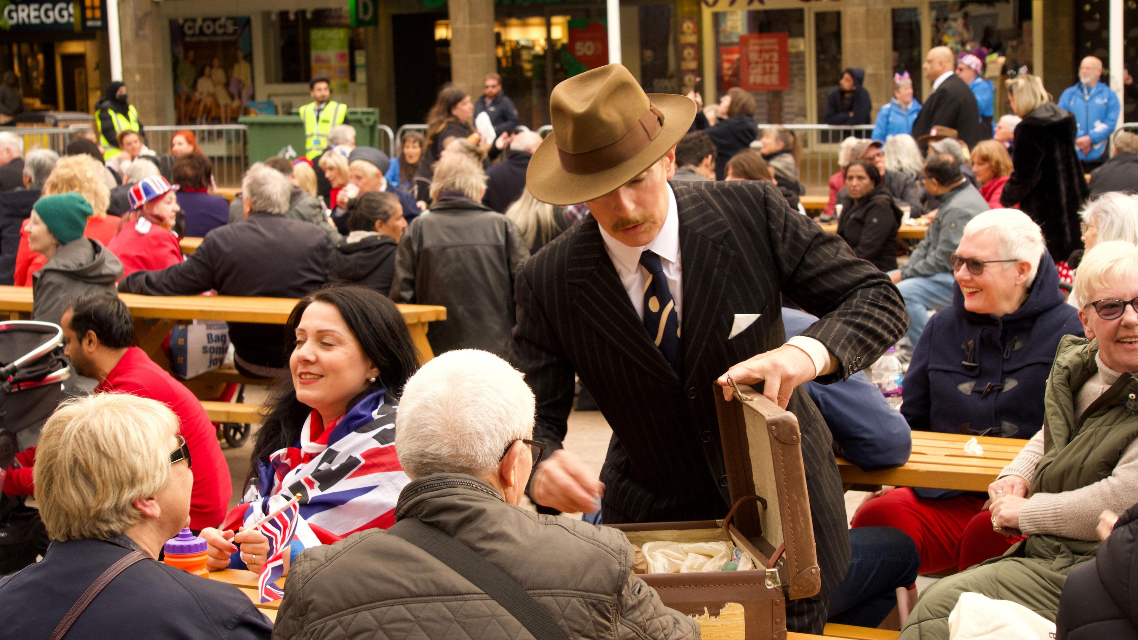 A man in a blue suit and blue tie and brown hat with a suitcase full of items that would not have been freely available during the war