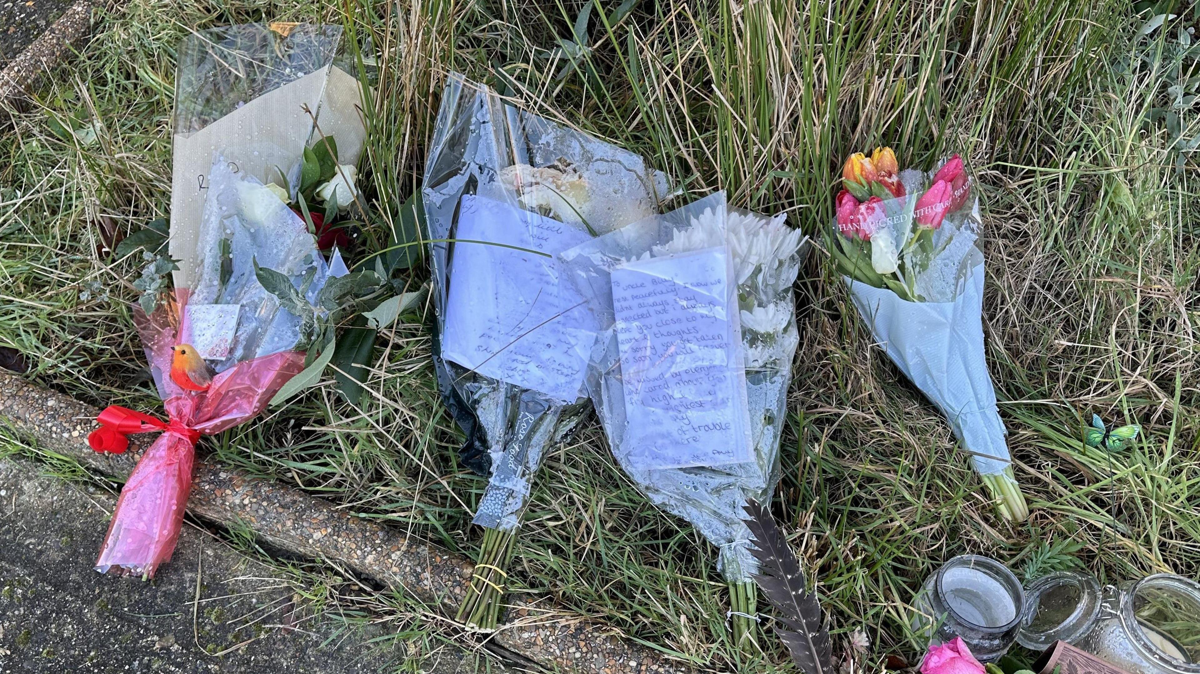 Flowers placed on a grass verge. Some have several notes attached to them in tribute to William McNicholl.