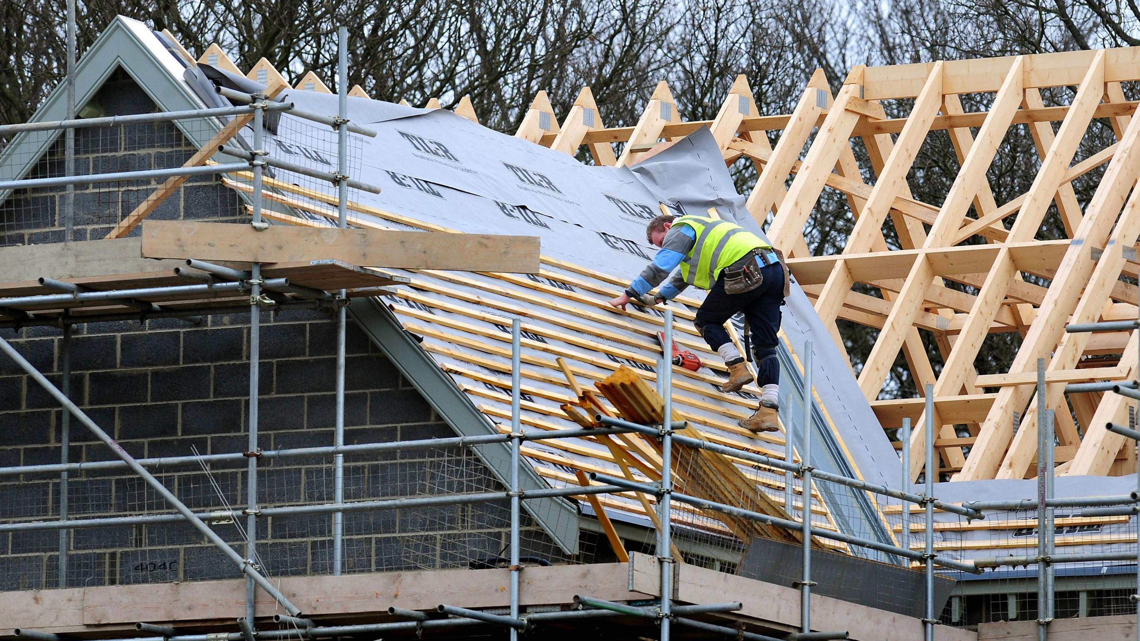 A roofer working on the roof of a newly-built house and wearing a hi-vis gilet and toolbelt