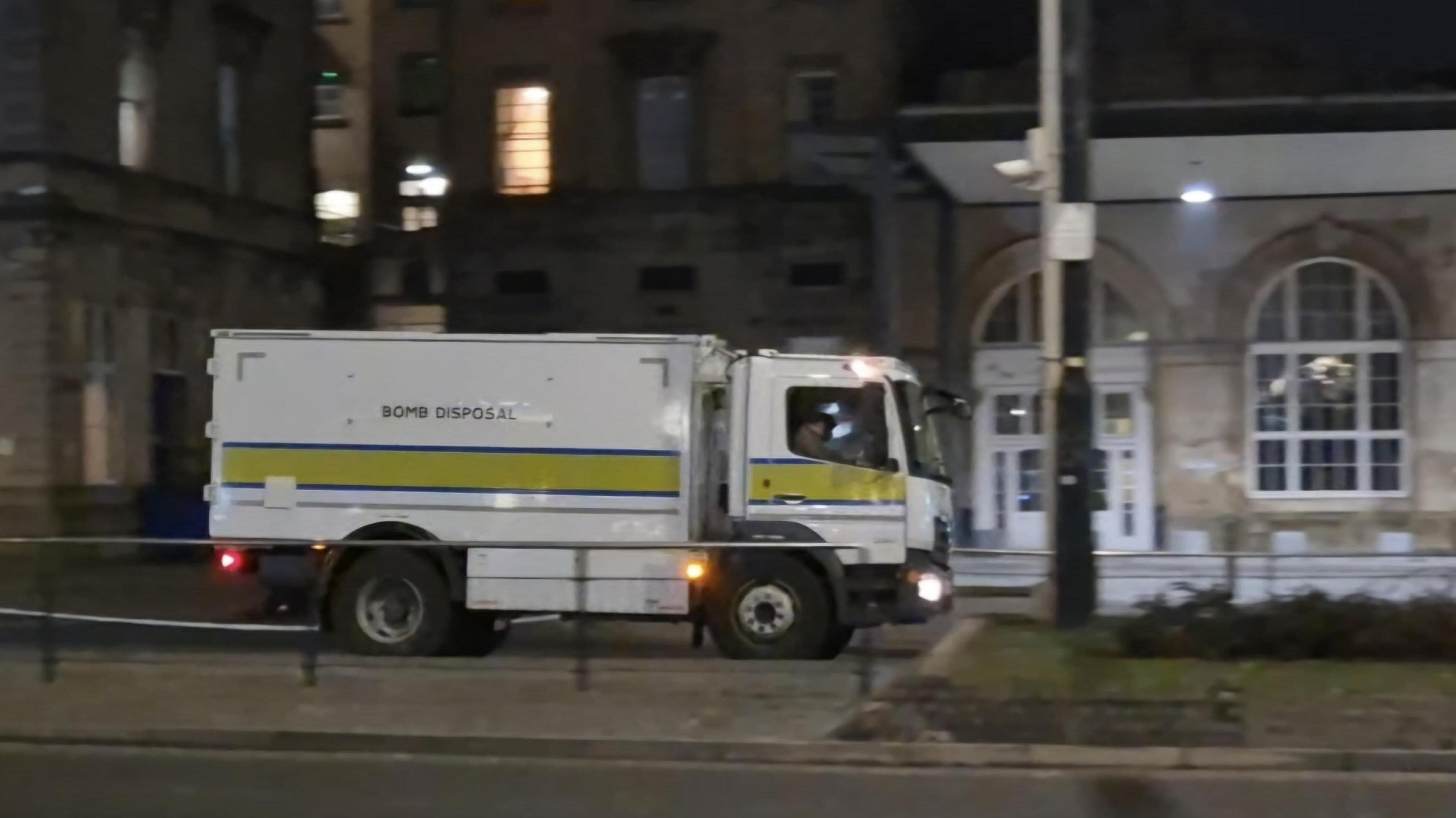 A white truck with the words "Bomb Disposal" written above a mustard-colour stripe on the side of vehicle.