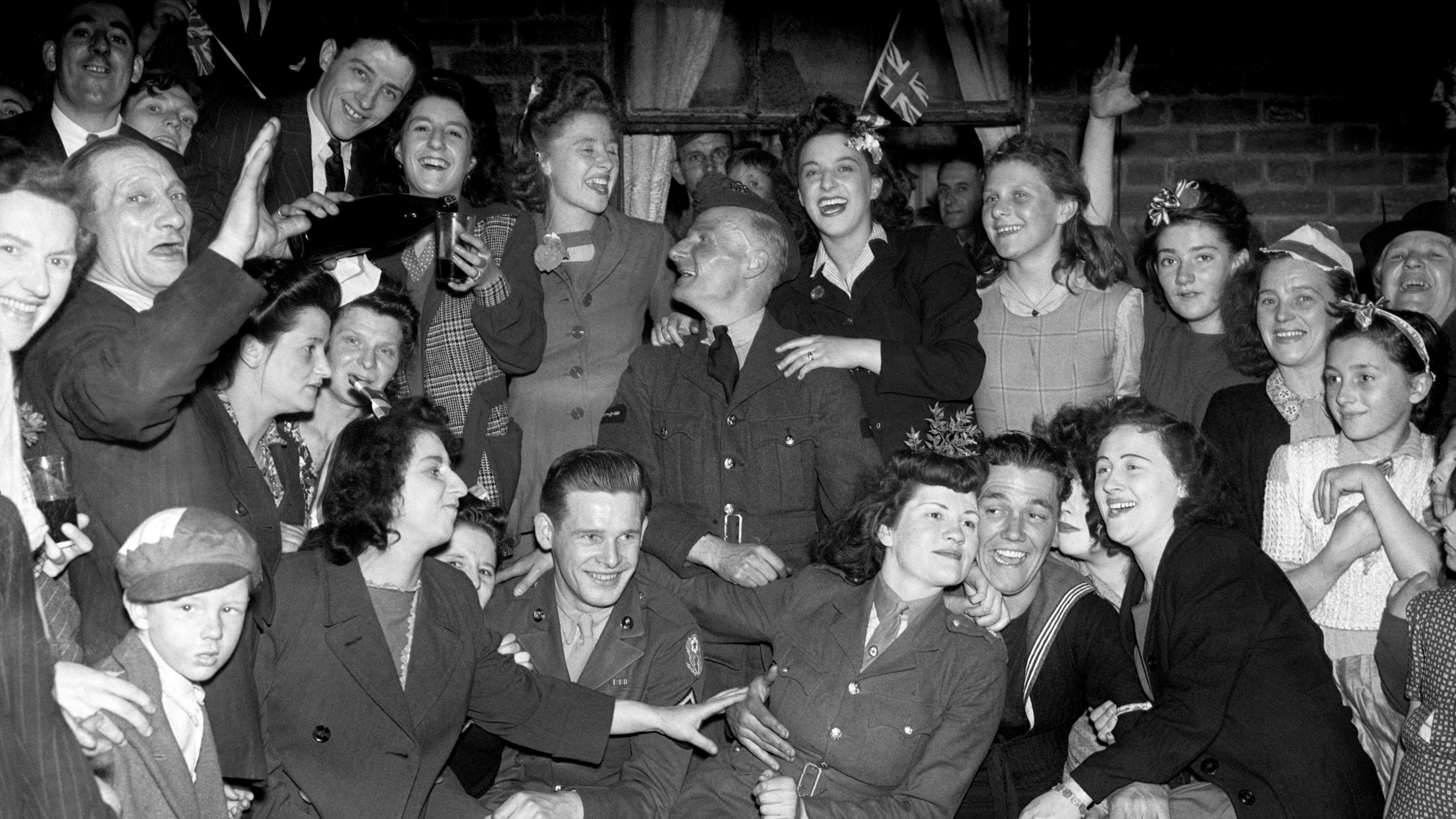 A crowd of people - young and old - gather to celebrate the end of the war in Europe. They are smiling as they huddle together for the photograph.