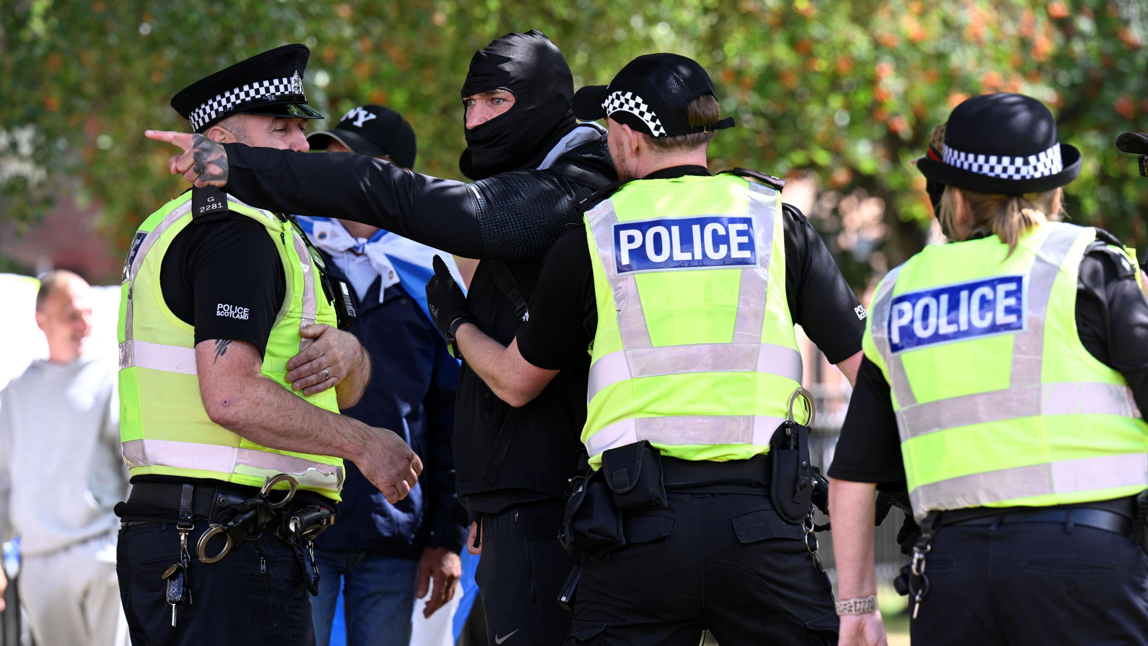 Police hold back a man wearing a black balaclava