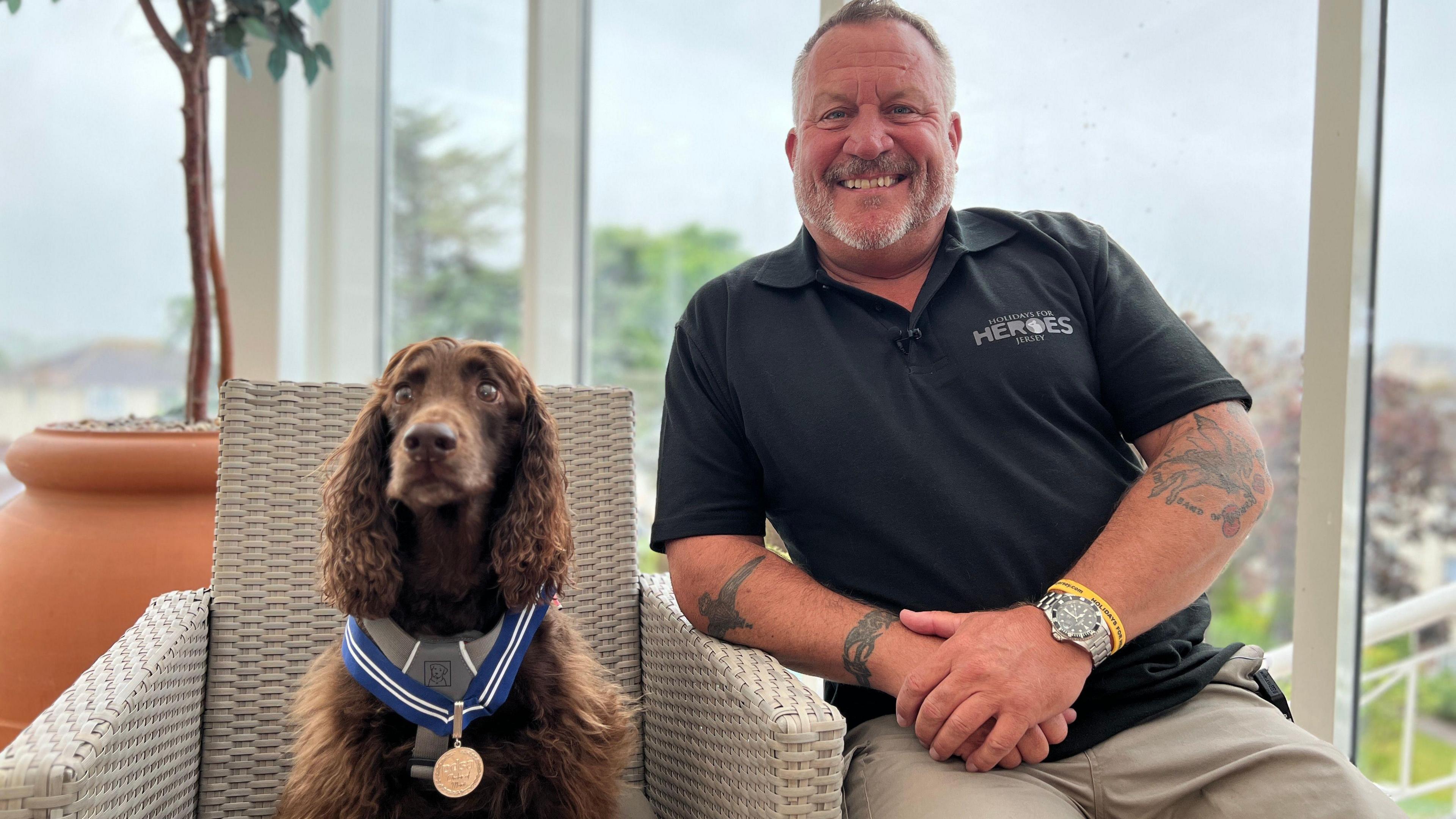 Mark smiles at the camera as he sits on a chair next to Jerry who is wearing his medal