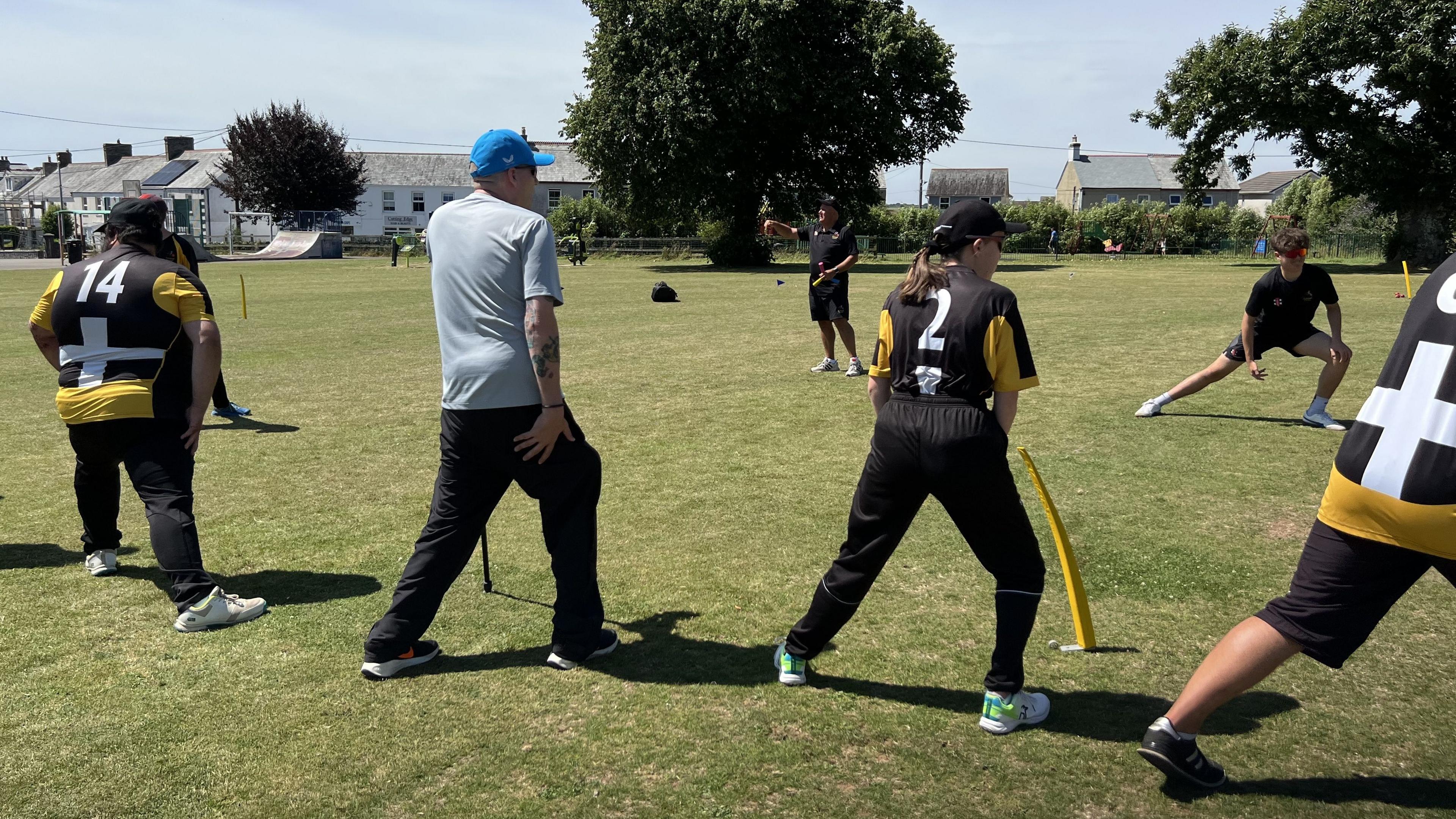 A group of cricketers with disabilities go through a stretching exercise wearing yellow and black kit 