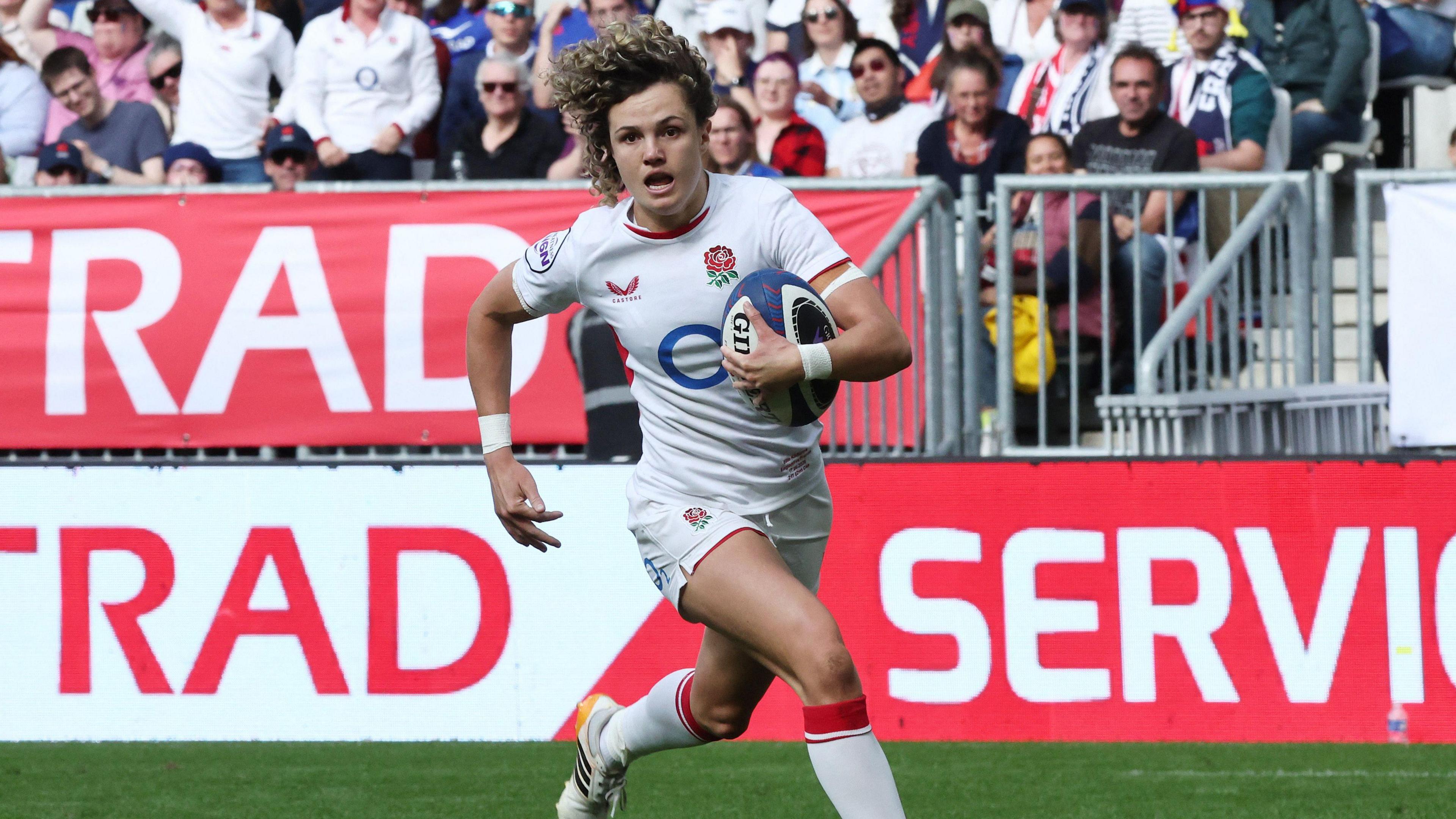 Ellie Kildunne running down the pitch rugby ball in hand with the crowd visible behind her