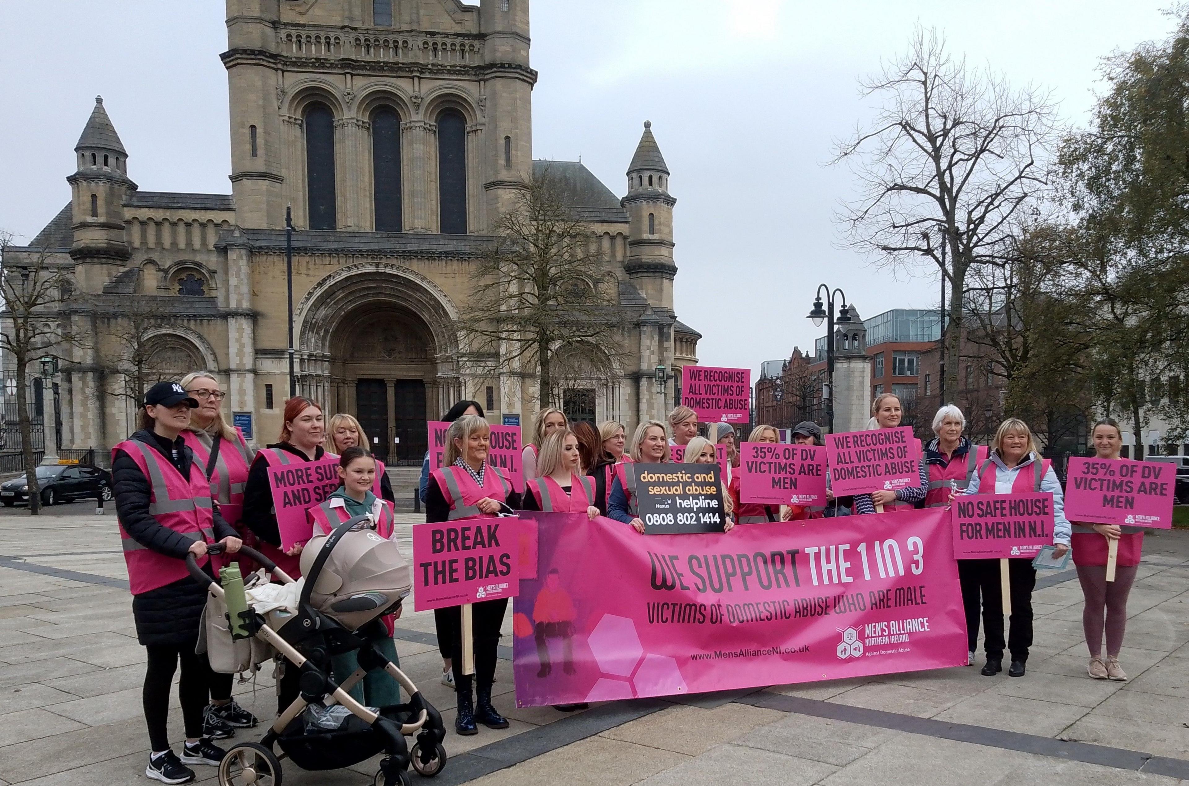 A group of women stand in Belfast wearing fluorescent pink and carrying banners and posters of the same colour.