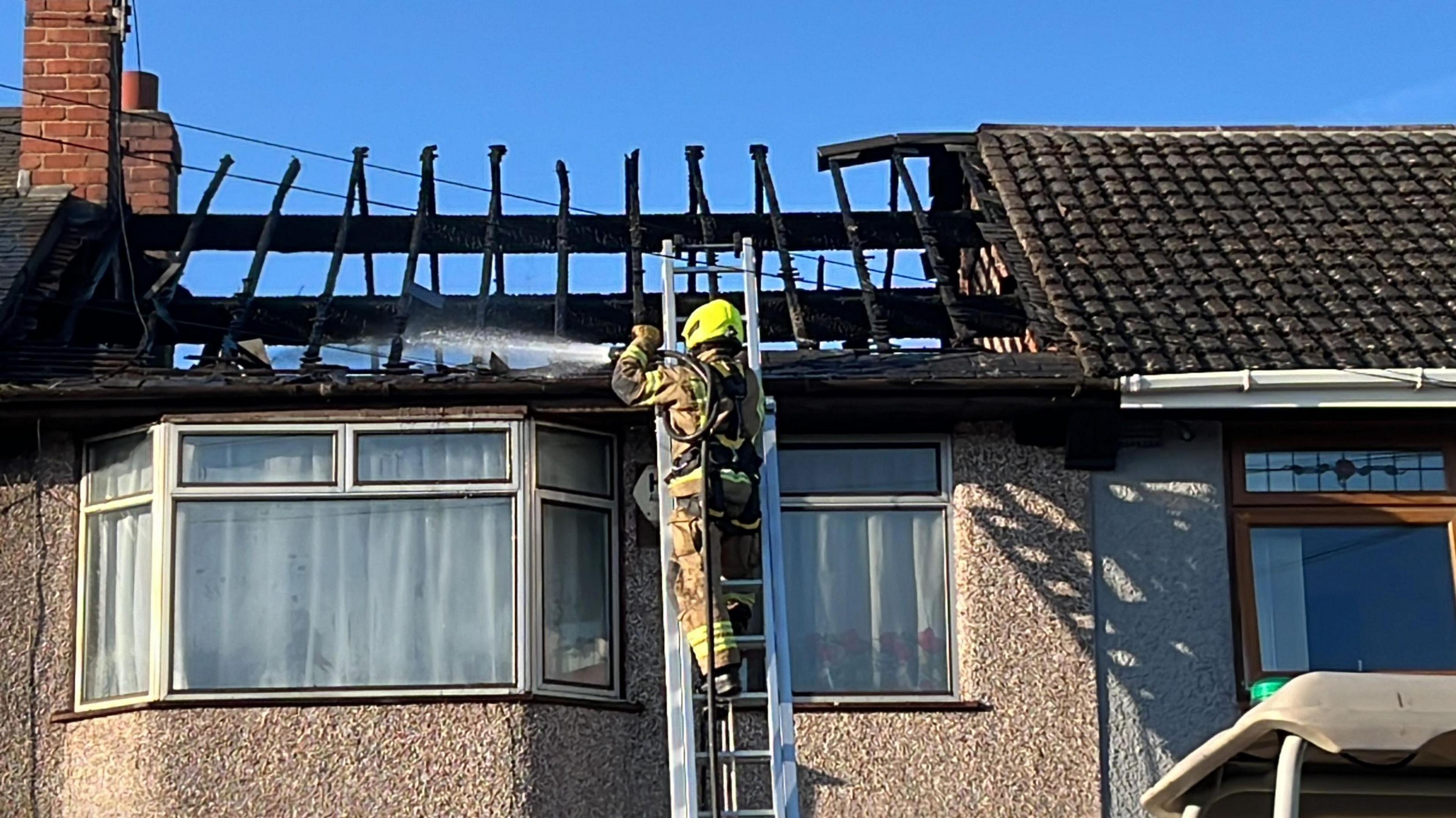 A firefighter spray water on the roof while standing on a ladder 