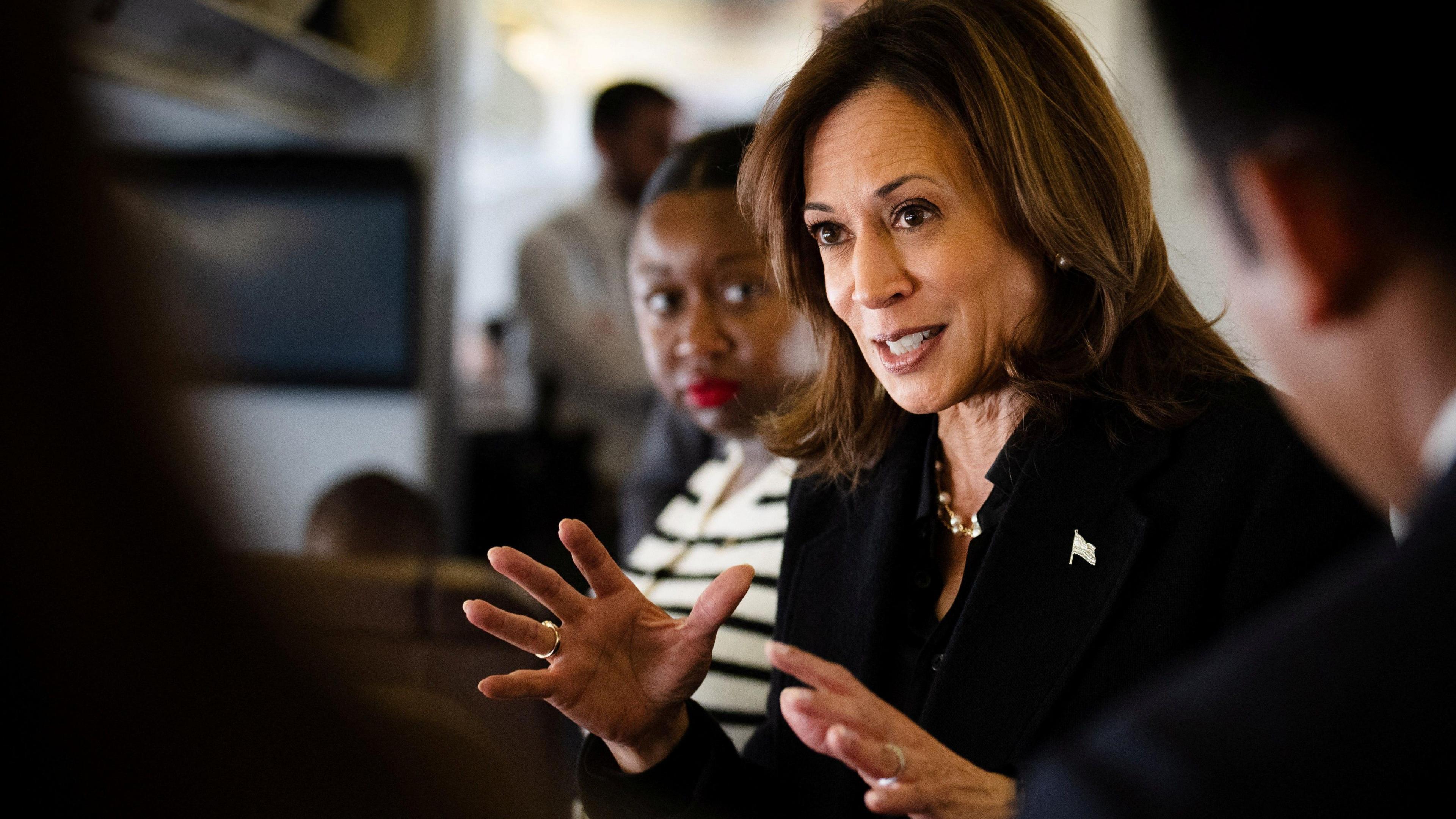 Democratic presidential nominee U.S. Vice President Kamala Harris talks to reporters using her hands while wearing a dark shirt. She is smiling and her face is seen at an angle.