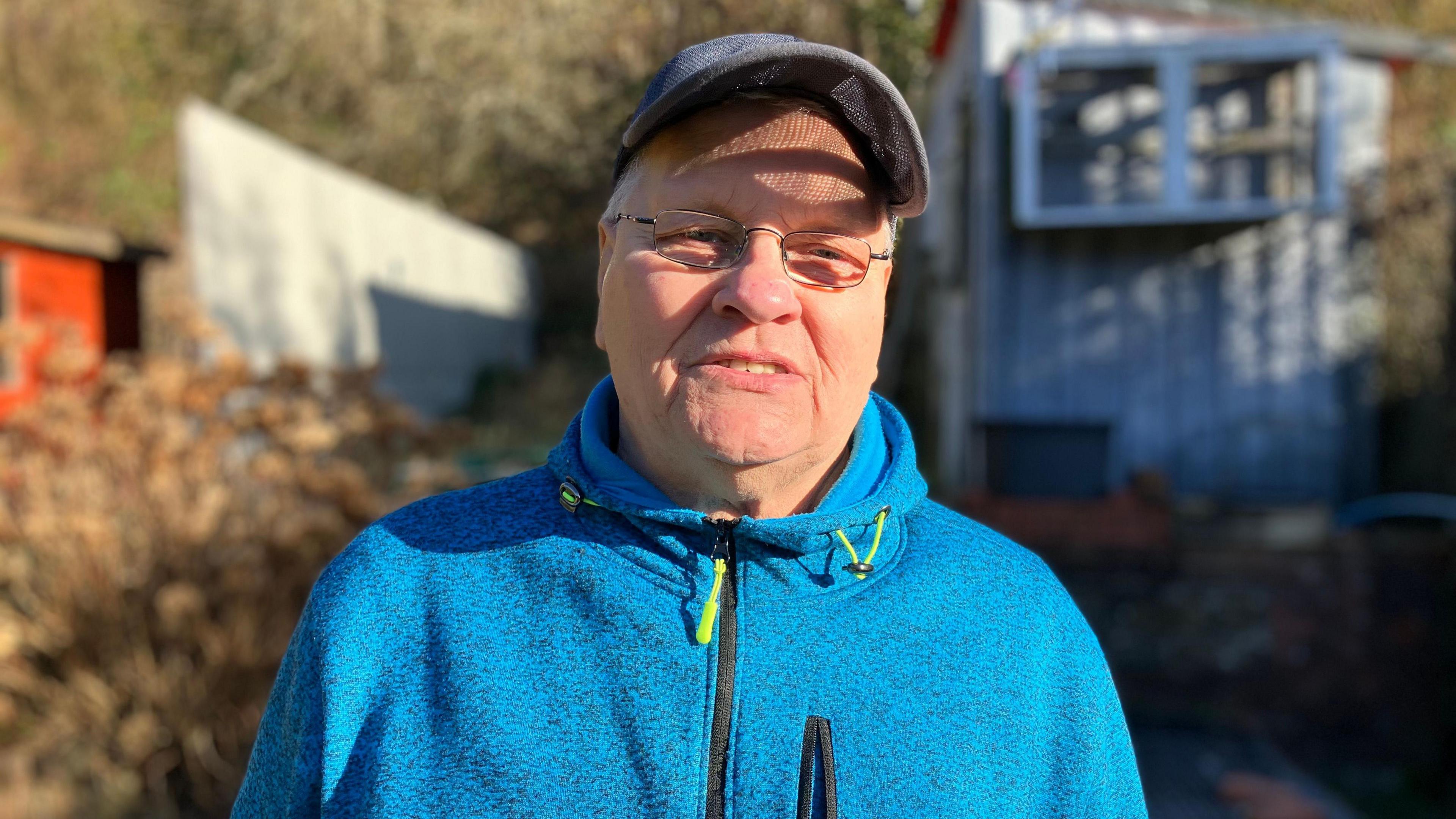 Brian Preece is wearing a blue hooded jumper and a baseball cap and is standing in his back garden, which backs on to the tip.