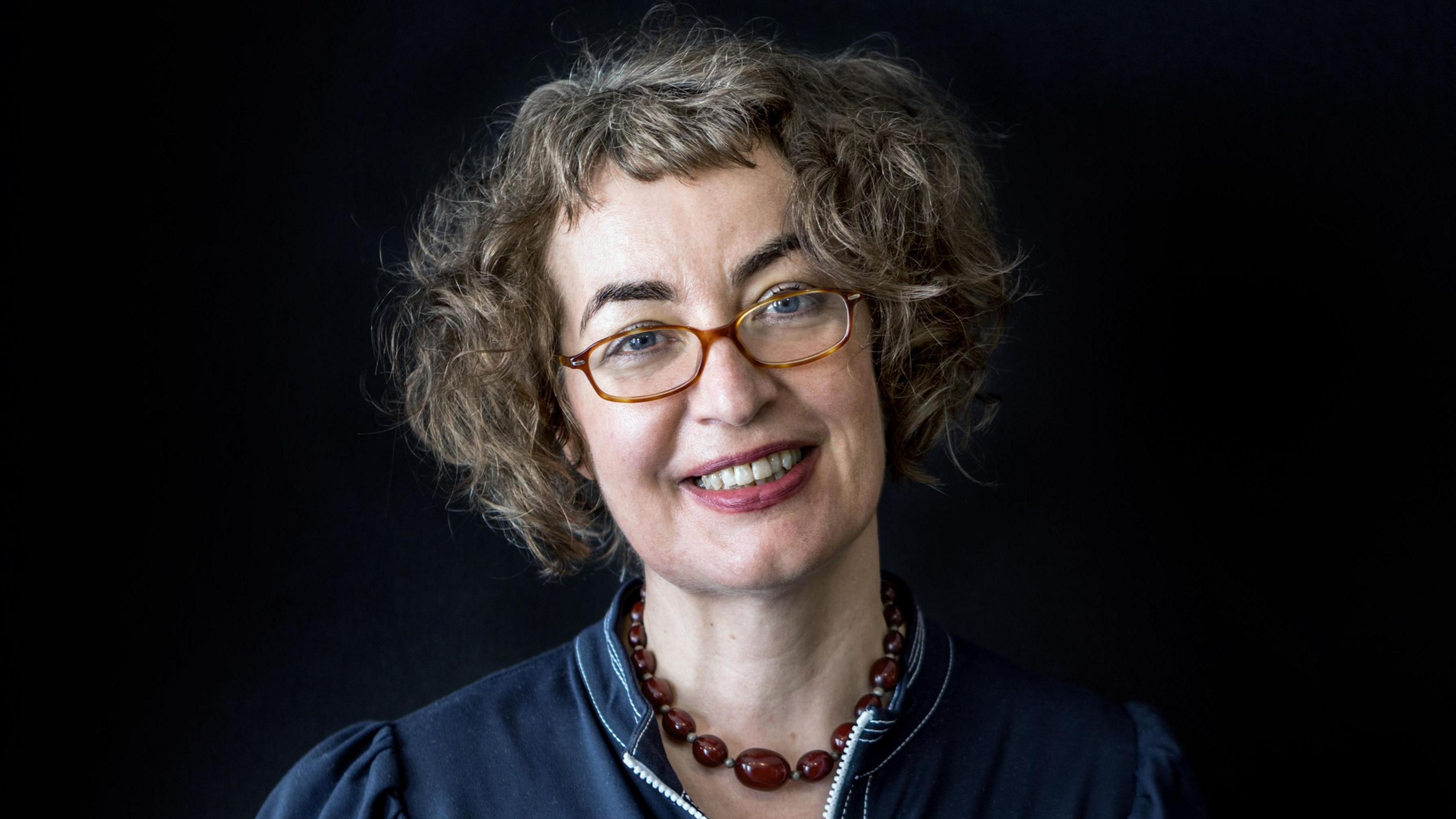 Kate Clanchy with glasses looking to camera. Brown beads around her neck.