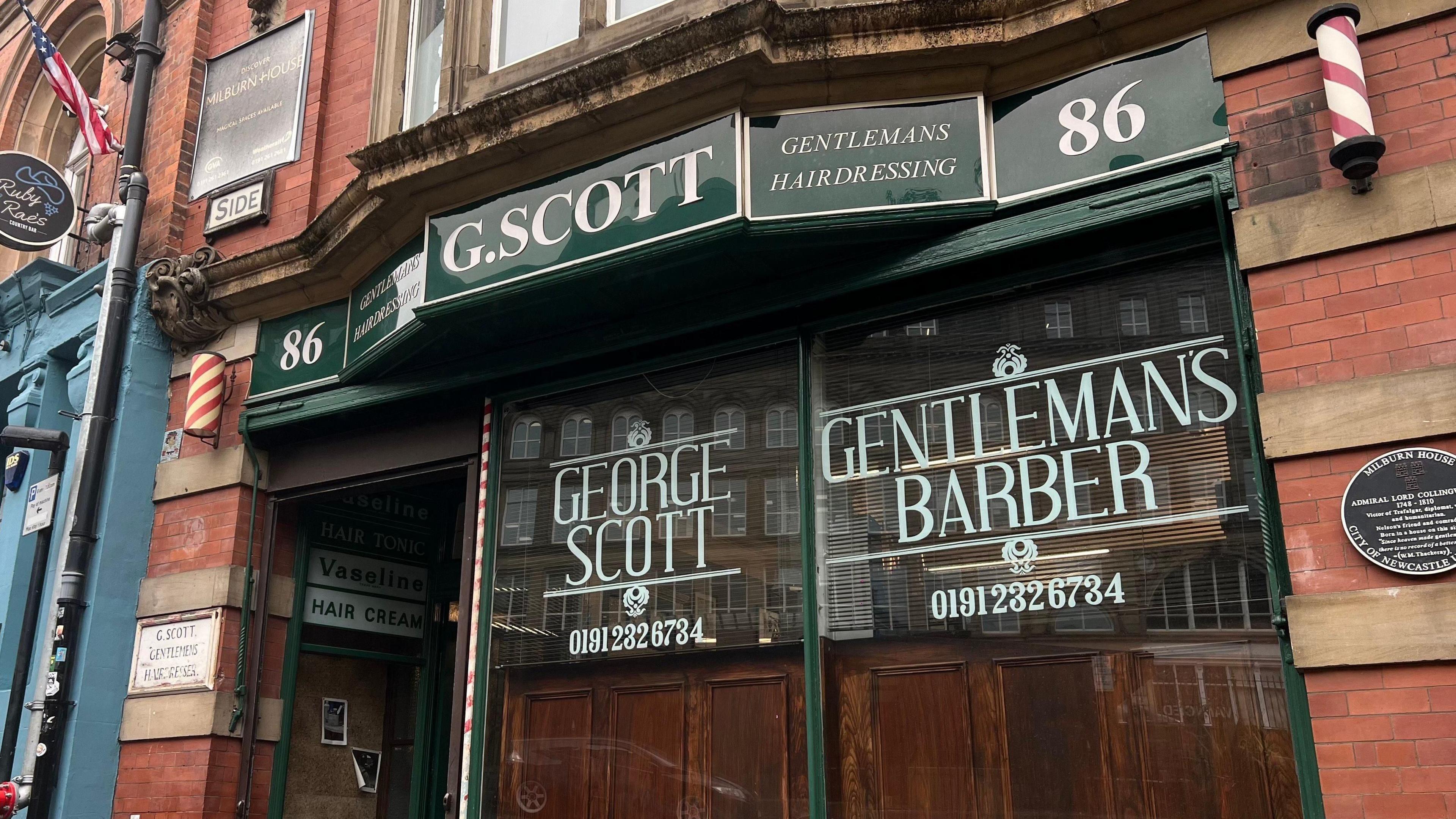 The outside of George Scott Gentleman's Hairdressers on The Side in Newcastle city centre. The exterior is painted dark green with white text painted on it.