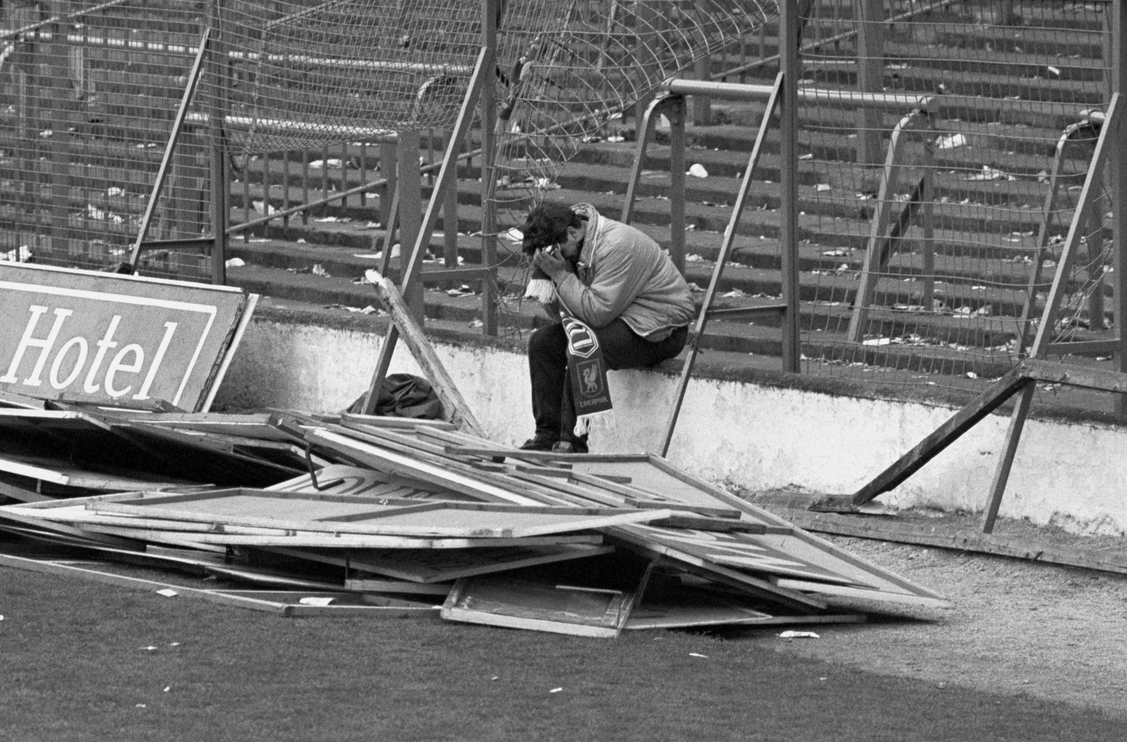 A single Liverpool fan sits among the damaged stands with his head in his hands