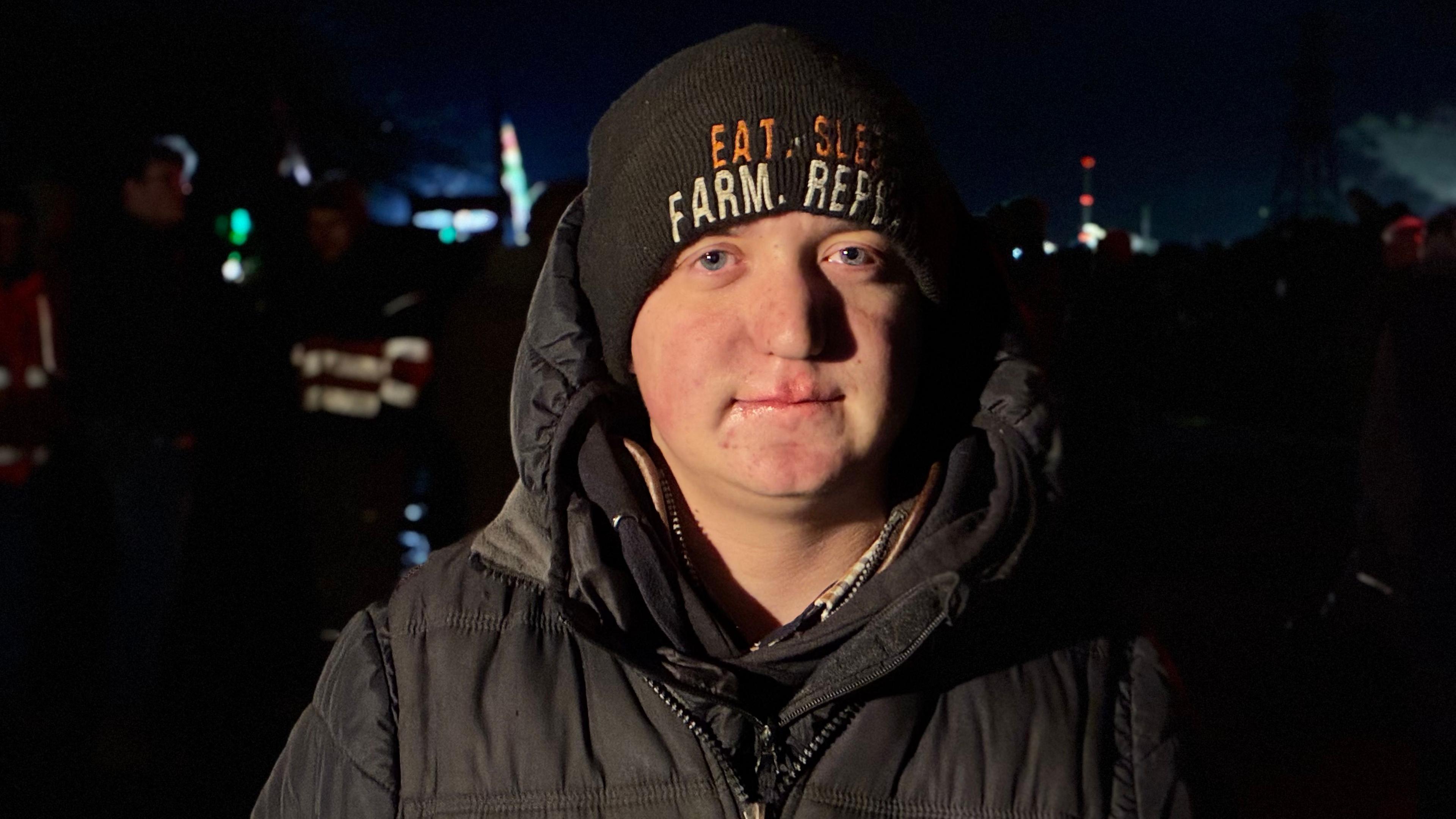 Head and shoulders shot of Jack Robinson, He is wearing a padded jacket and a beanie hat with orange and white writing on it.