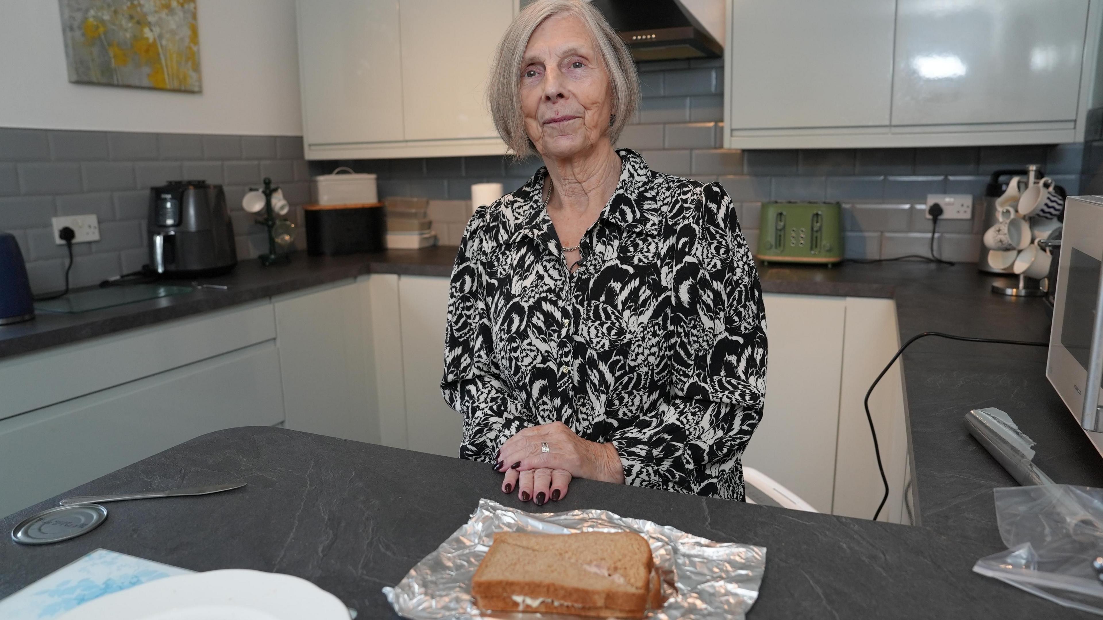 Dorothy standing in a kitchen with a tuna sandwich in foil on the work surface in front of her