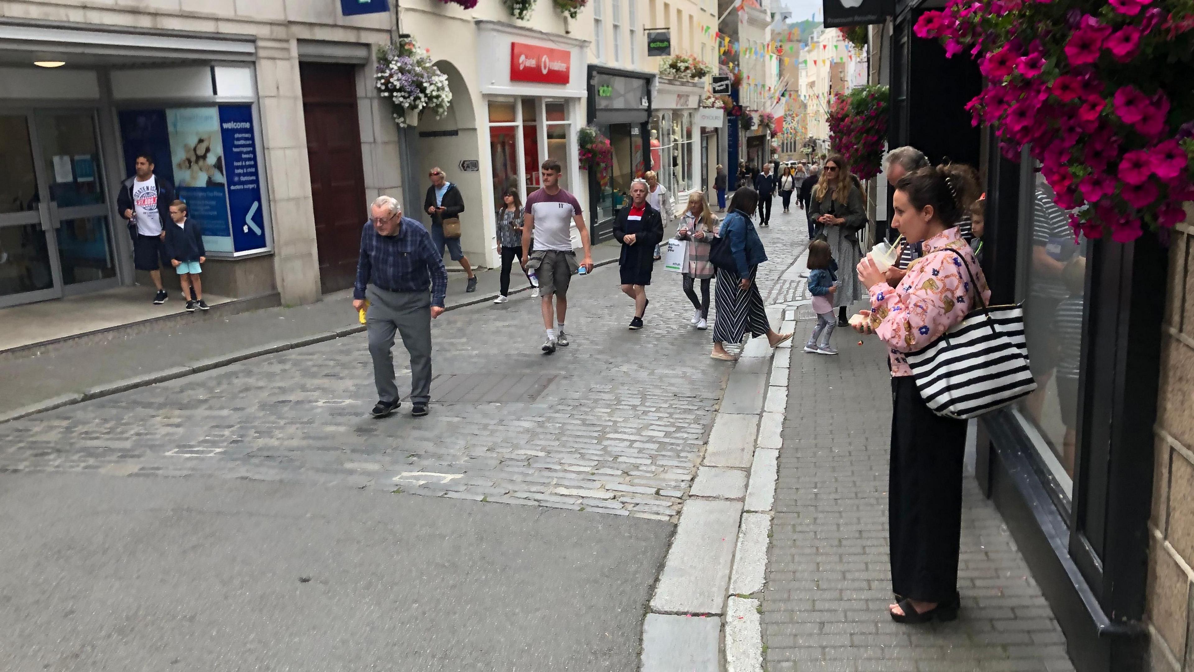 Guernsey's High Street - a grey high street, with cobbles in the middle and shops on either side. People are walking back and forth.