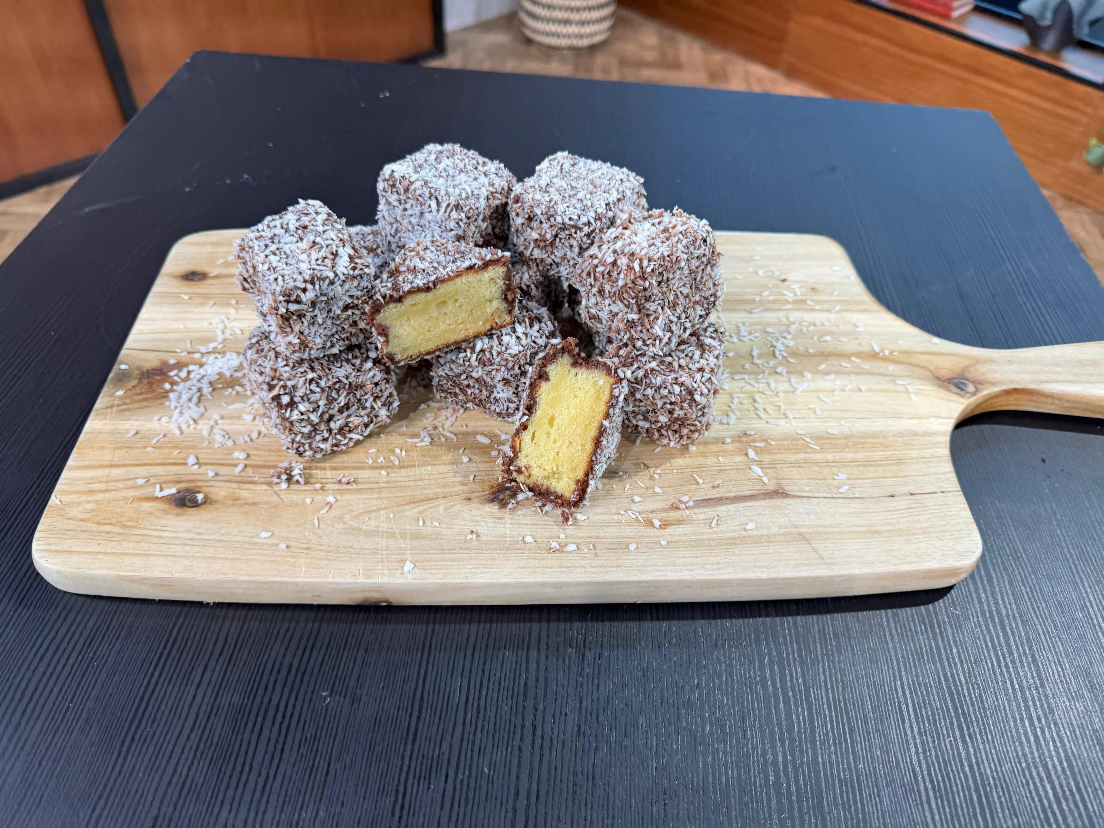 8 lamingtons on a chopping board with coconut sprinkled around