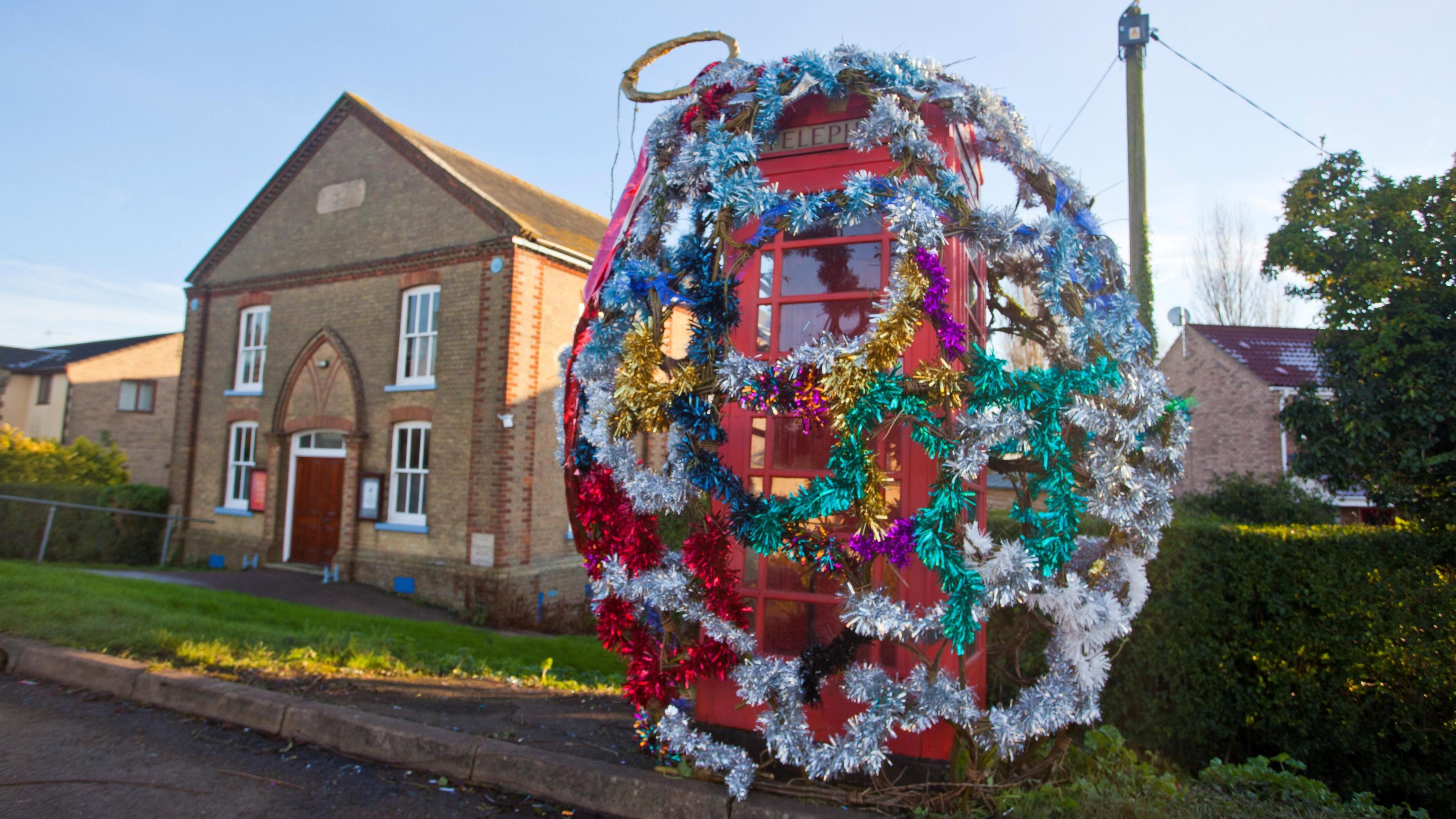 A red phone box completely covered with colourful tinsel in the shape of a Christmas bauble