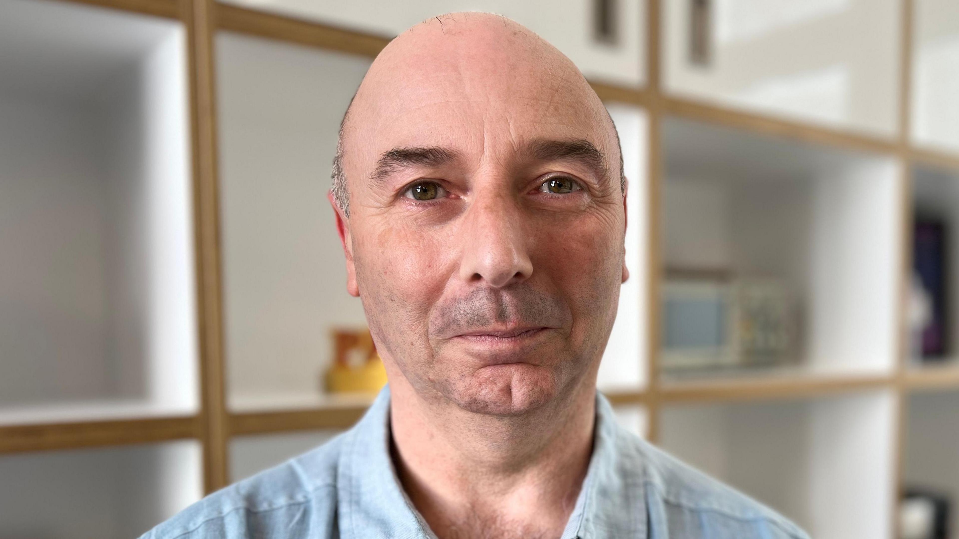 Giuseppe Capanna looking into camera. He is wearing a pale shirt with a collar and there are shelves visible behind him