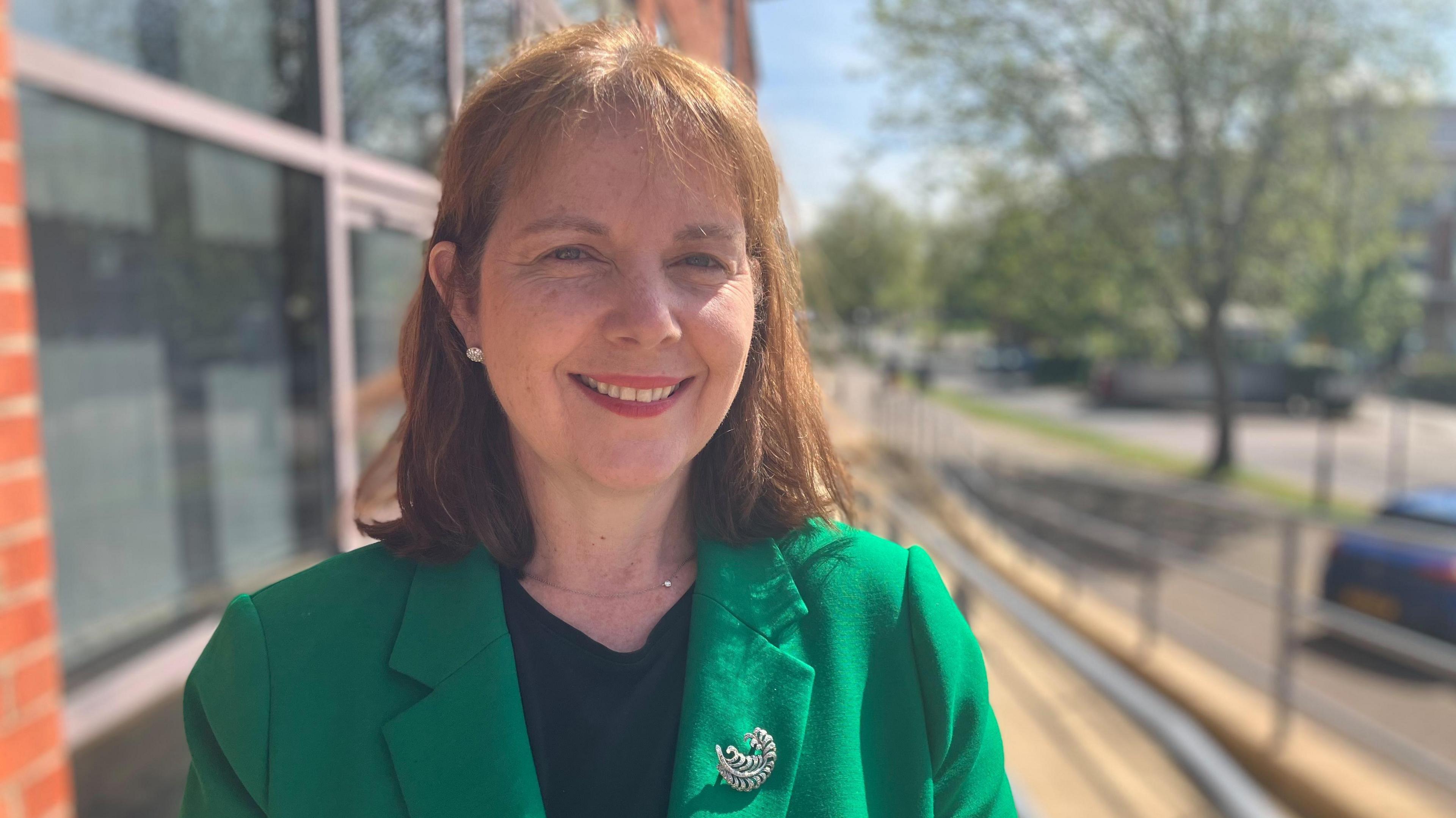 East Midlands mayor Claire Ward stood outside a building smiling wearing a green blazer and silver broach