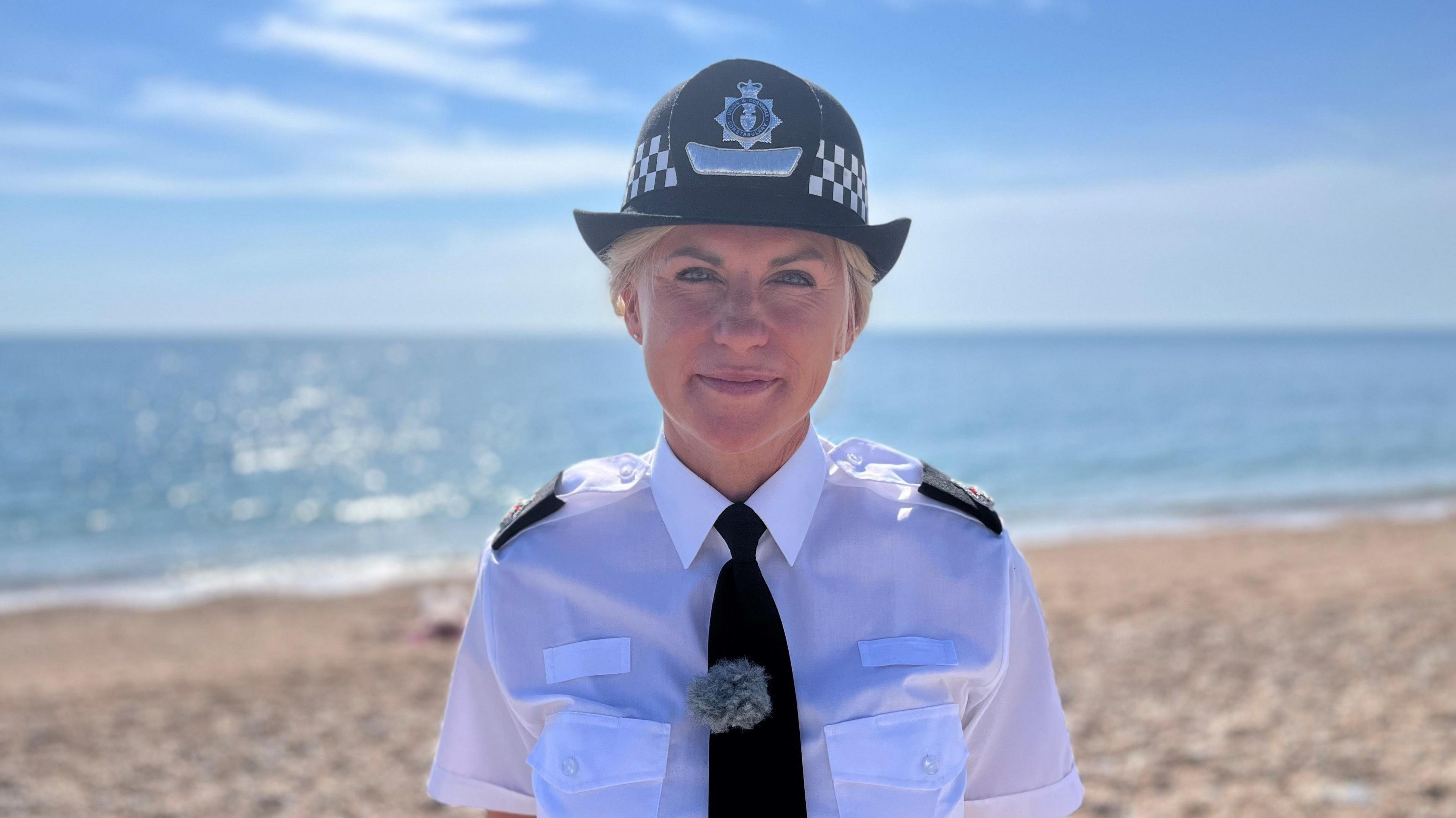 Det Supt Alex Doughty, strategic lead for organised immigration crime at Devon and Cornwall Police, standing on a beach in a police uniform, including hat 