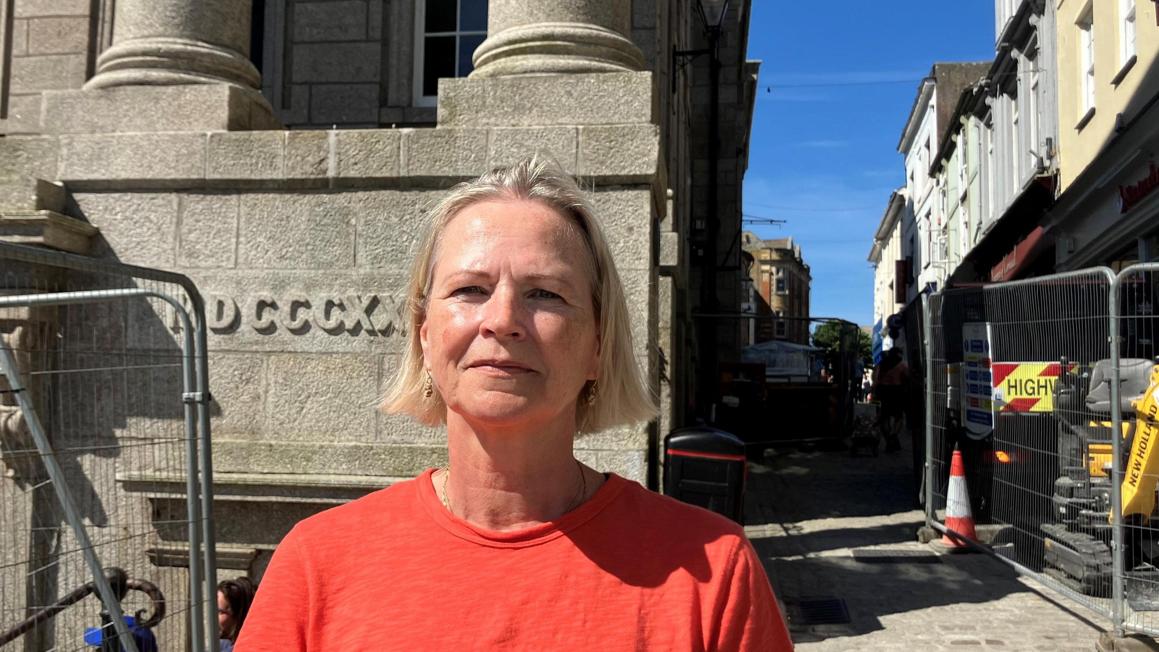 A woman stands in the middle of Penzance, she wears an orange T-shirt