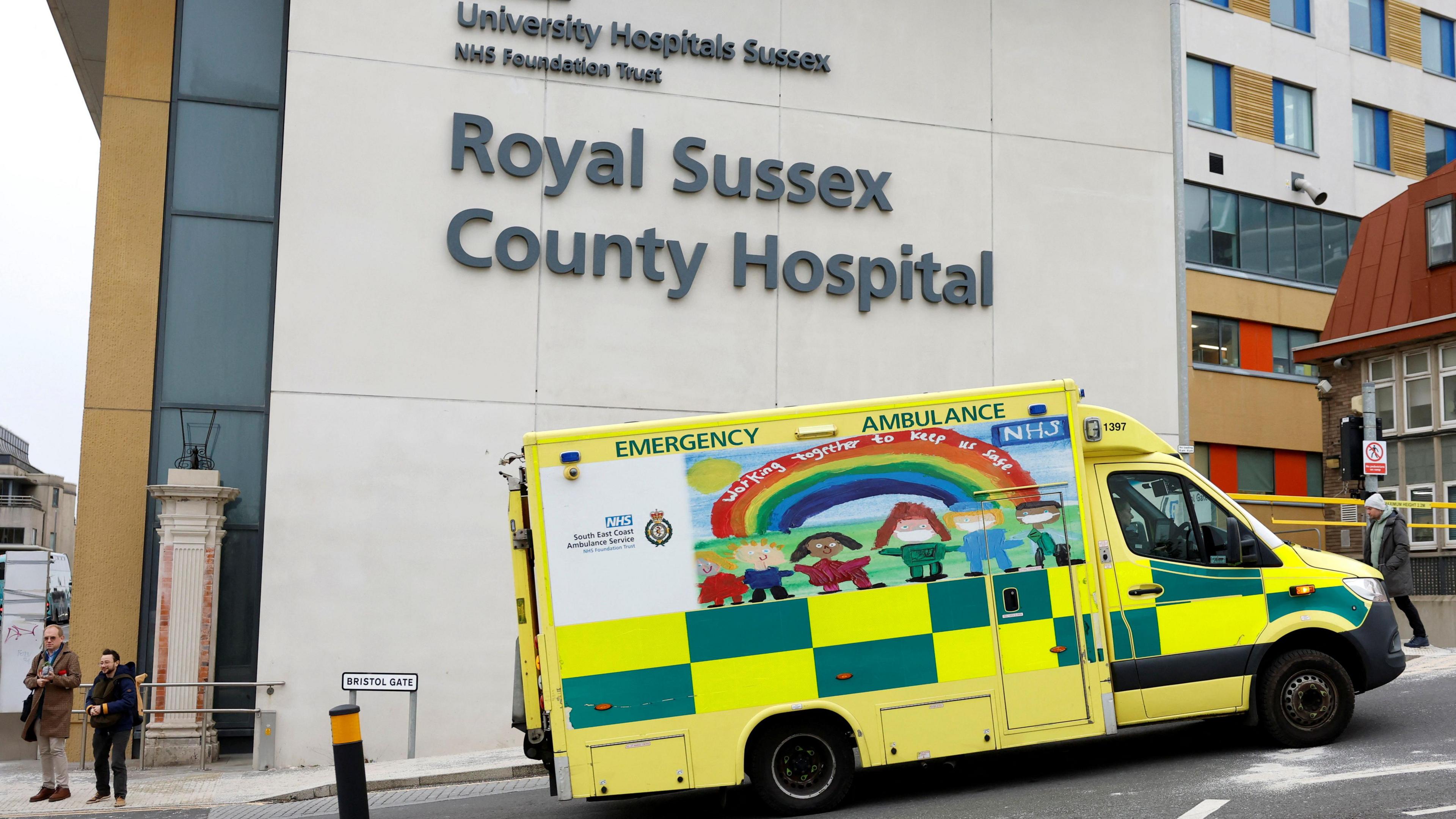 An emergency ambulance driving past a hospital building signposted Royal Sussex County Hospital